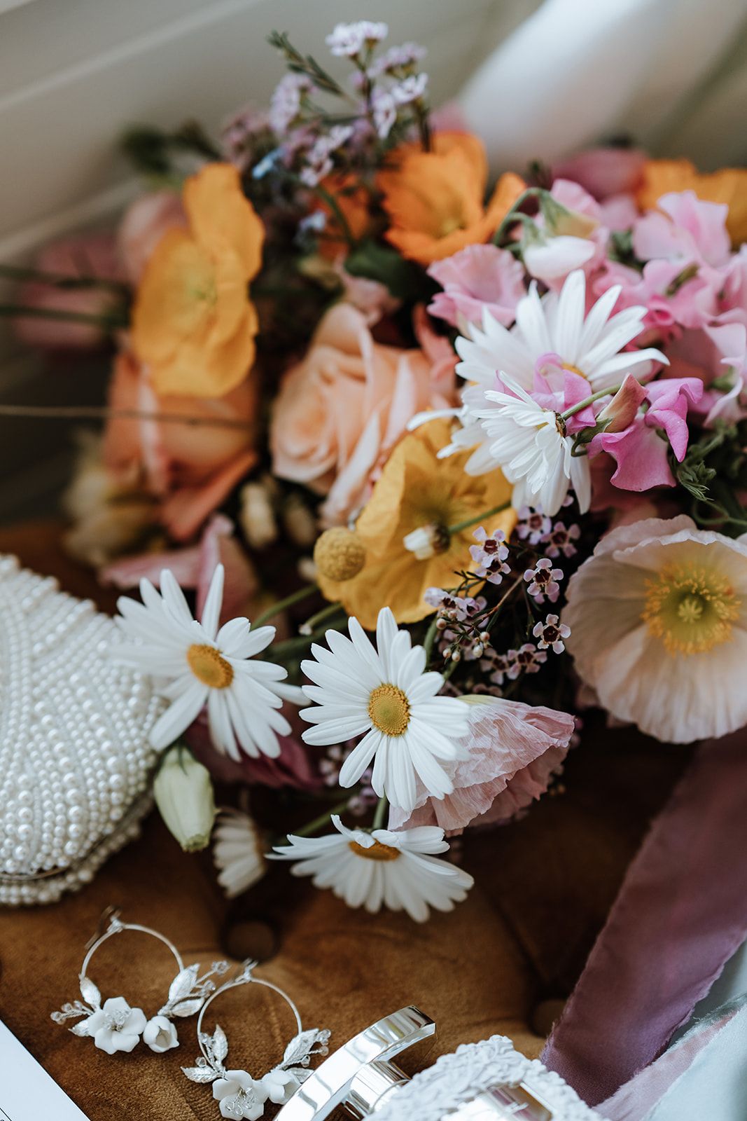 Wedding bouquet with daisies, pink and orange flowers, pearl accessories on a brown velvet surface.