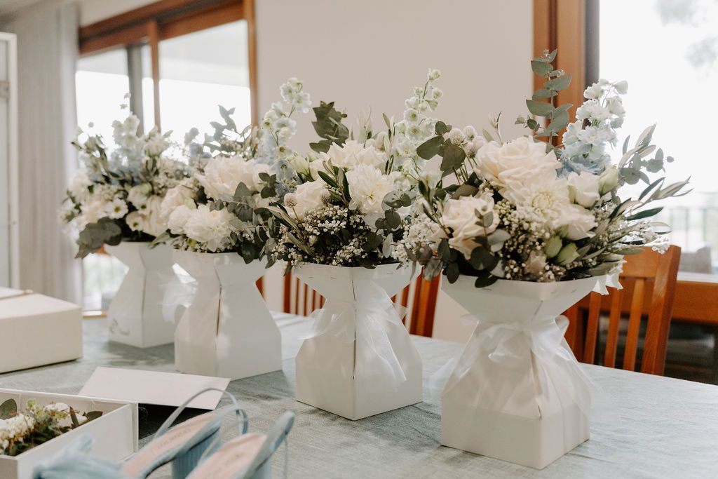Four white and blue floral bouquets in unique, white vases on a table.