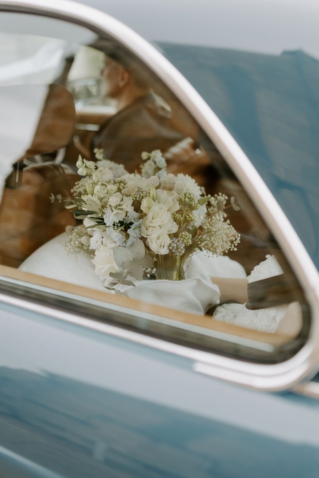 Blue car window with a white floral bouquet inside.