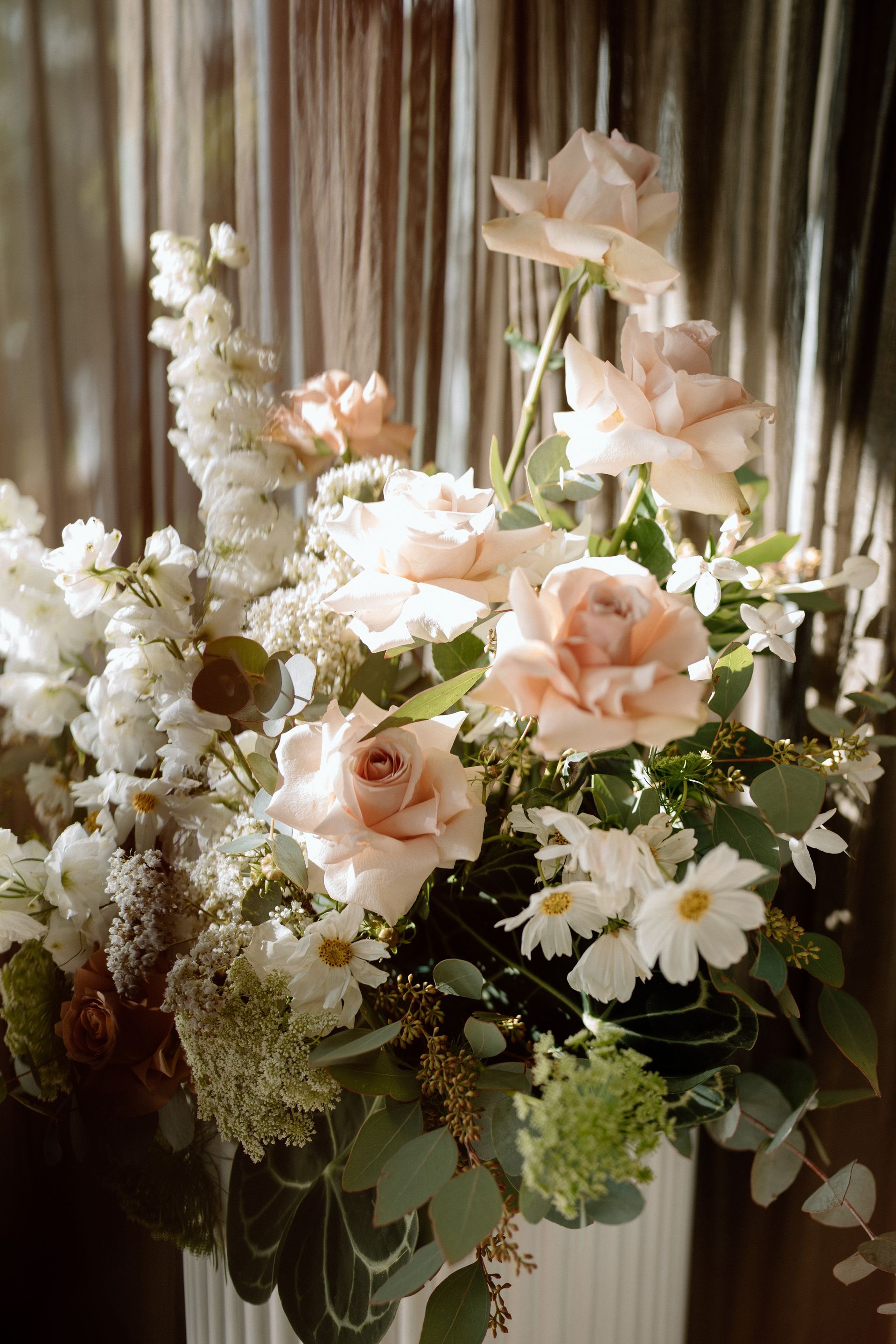 A bouquet of light pink roses, white daisies, and green foliage in a white vase.
