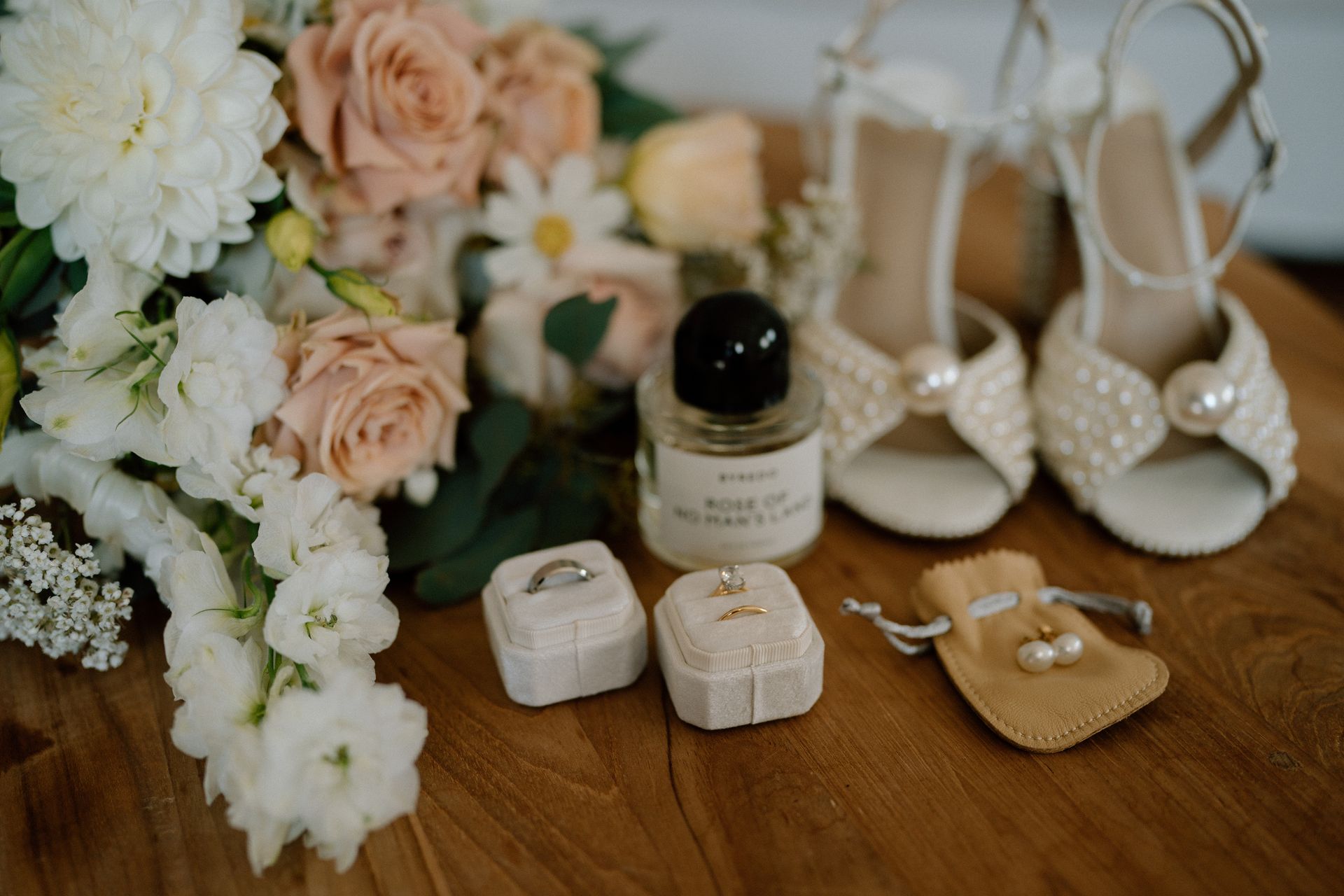 Bridal details: bouquet, pearl-embellished heels, rings in boxes, perfume, and small pearl earrings.