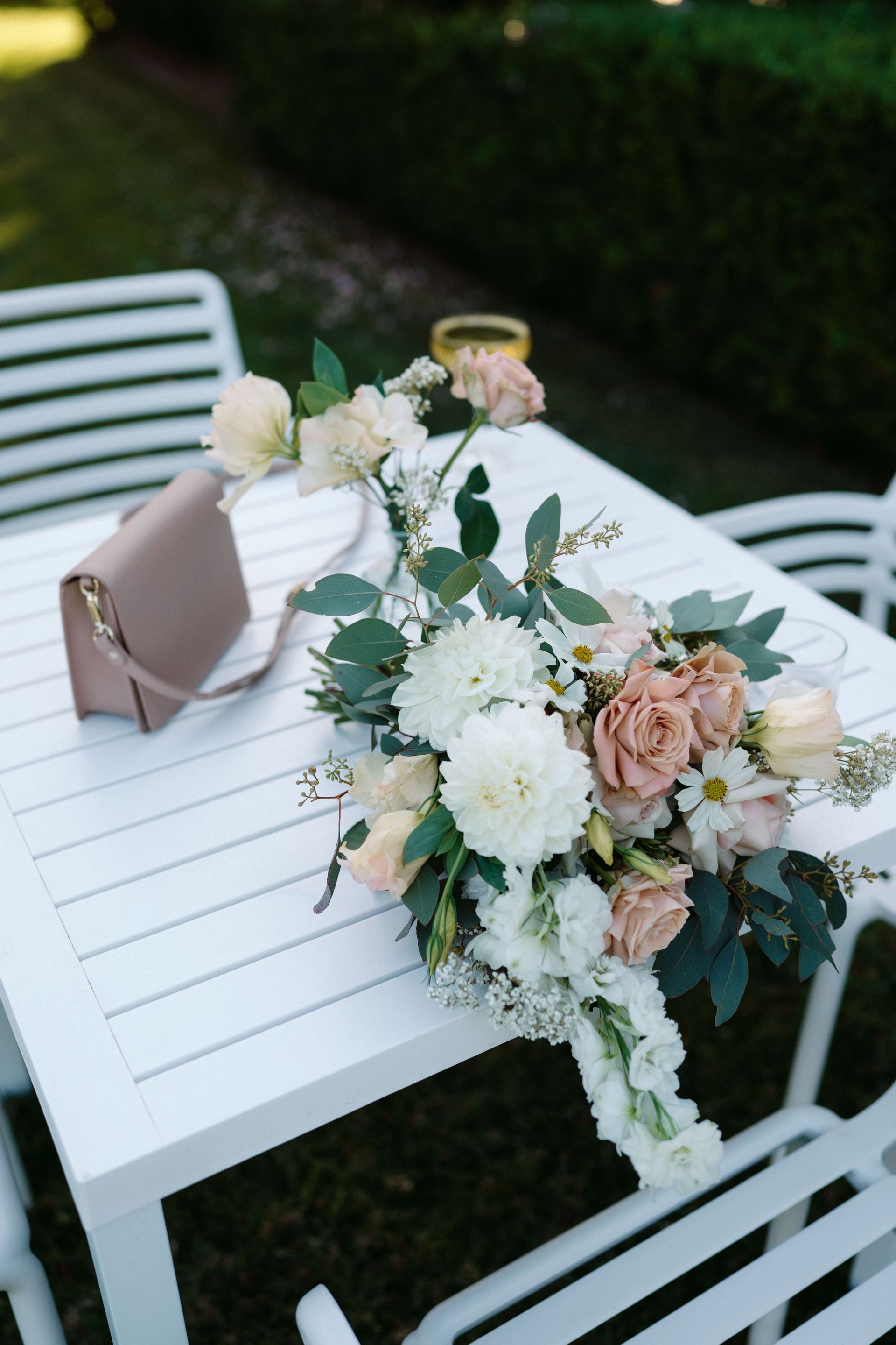 Bouquet of white and peach flowers on white table with a purse. Outdoors.