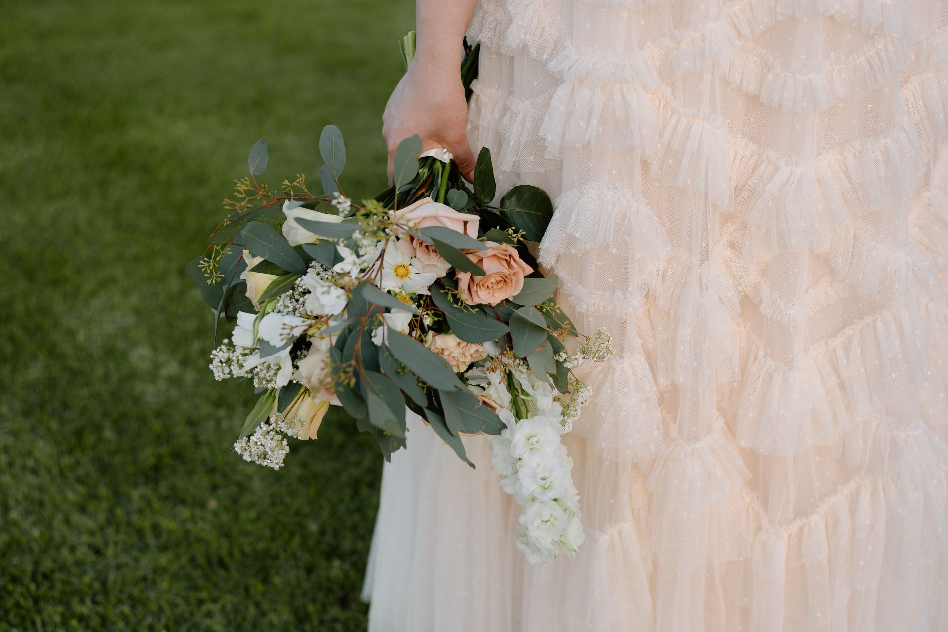 Bride in a ruffled dress holding a bouquet with white, peach, and green flowers.