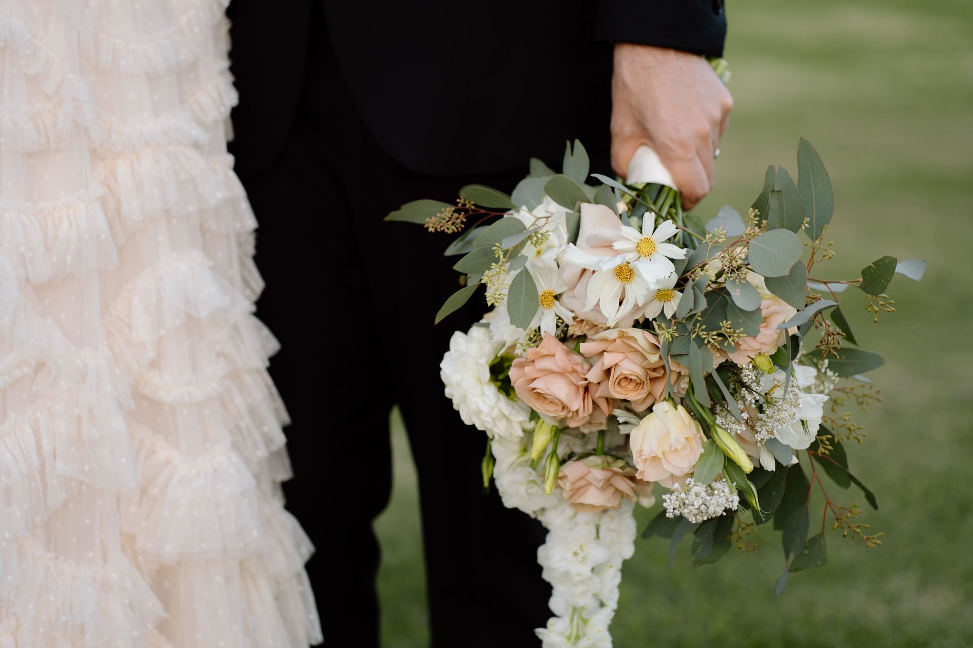 Bride and groom hold a bouquet of flowers, showing the bride's dress and groom's suit.