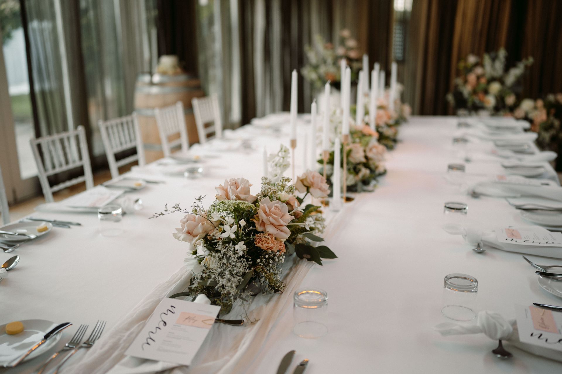 Long rectangular table set for a formal event with white tablecloth, floral centerpieces, candles, and place settings.