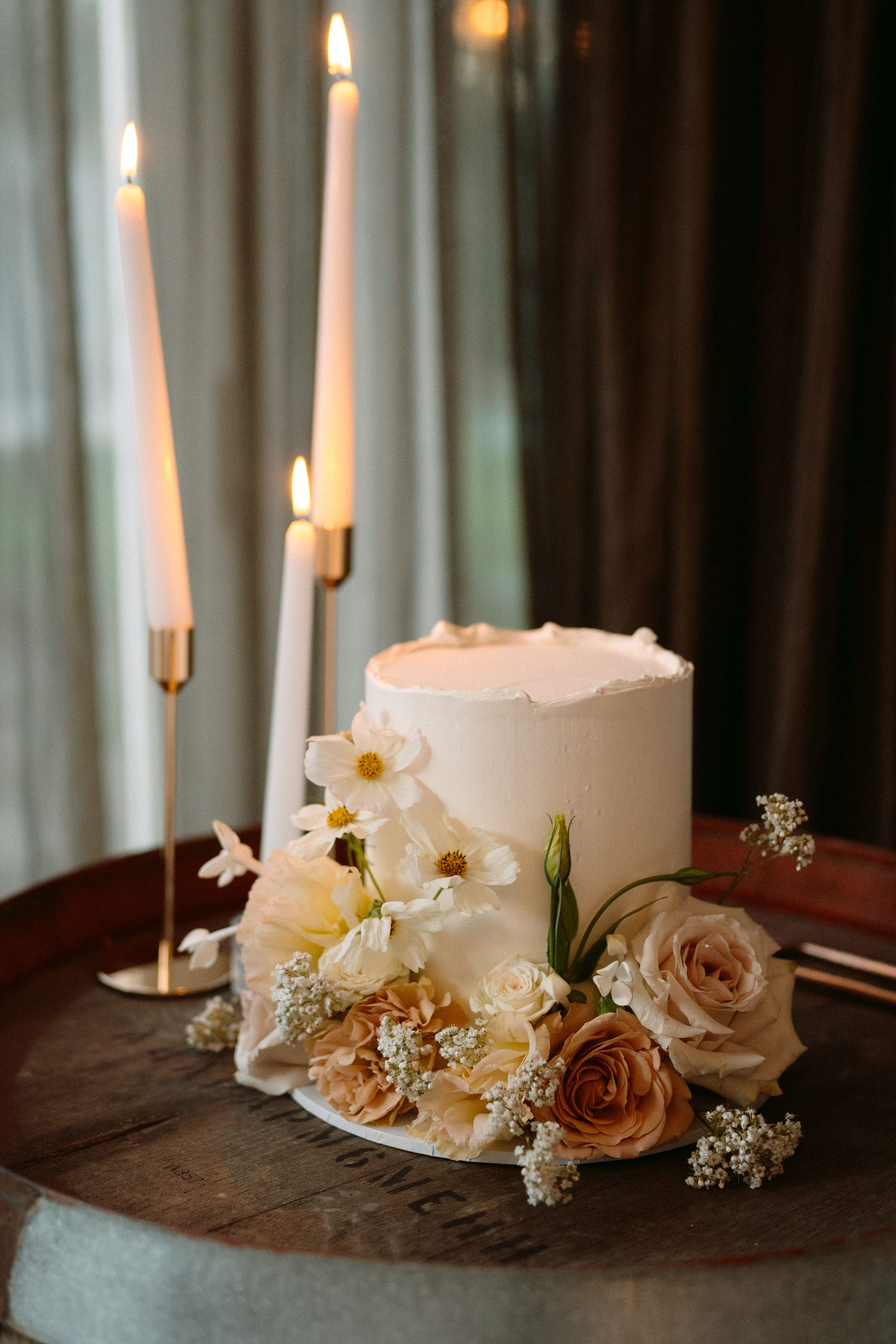 Wedding cake with flowers and lit candles on a wooden tray.