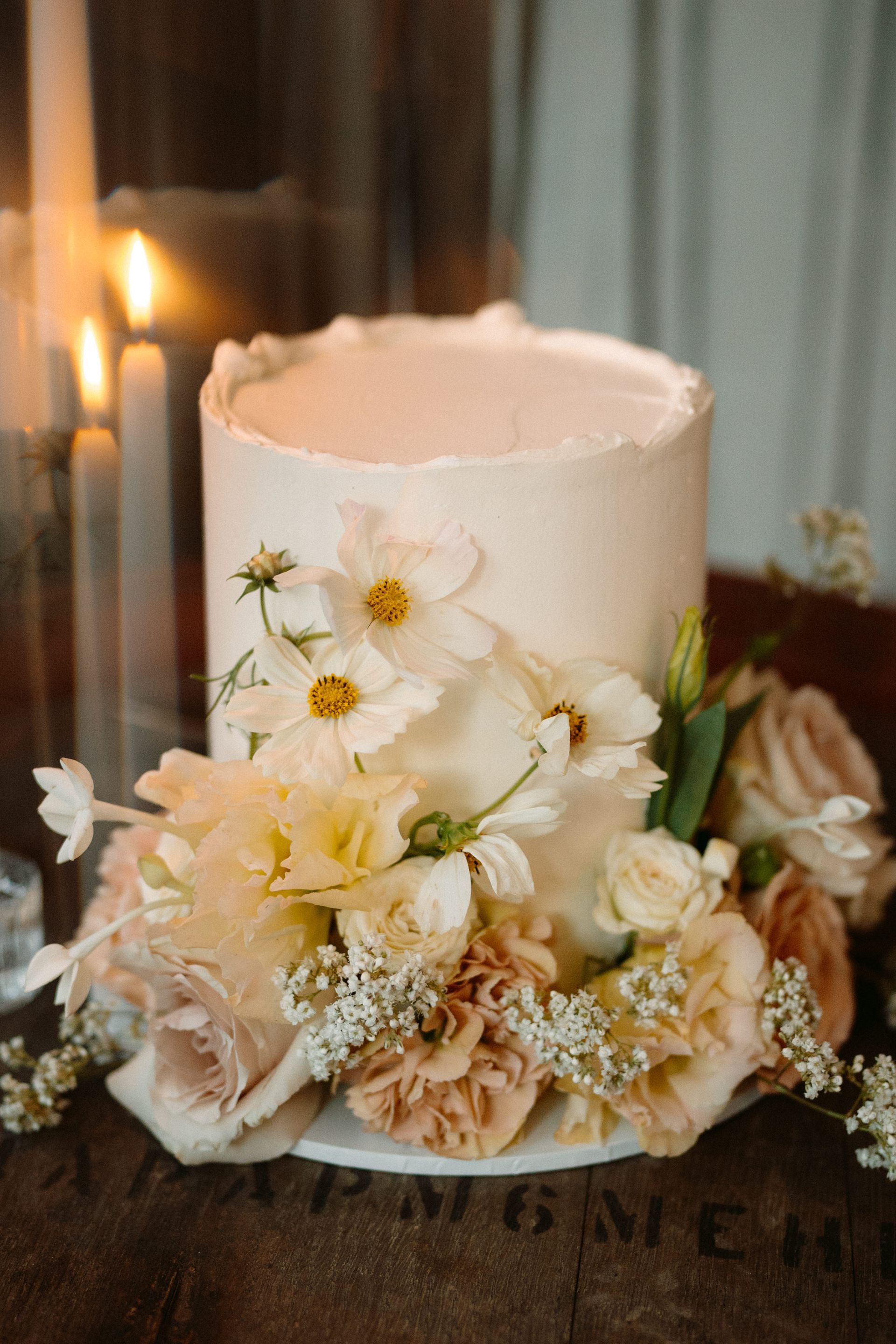 Wedding cake with white frosting, surrounded by light-colored flowers and greenery.
