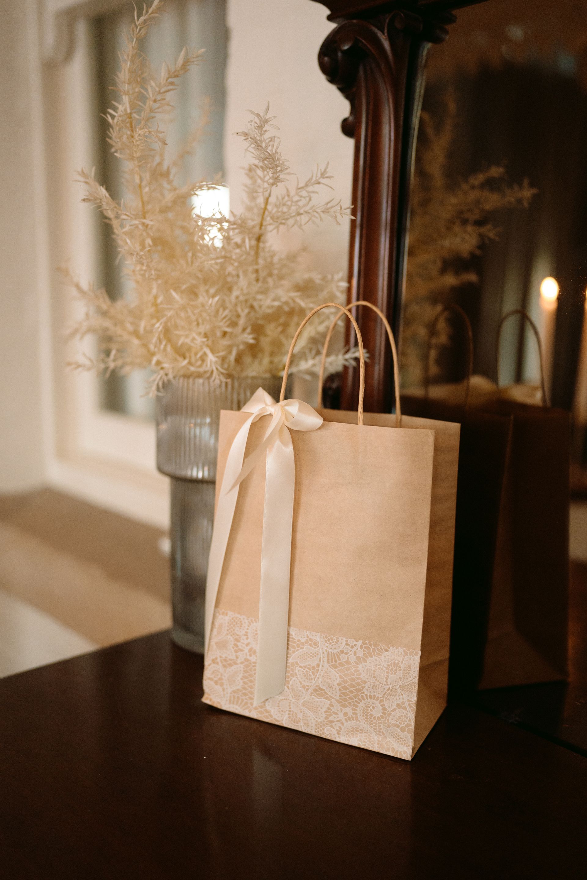 Brown paper gift bag with a cream ribbon bow, next to a vase of dried flowers.