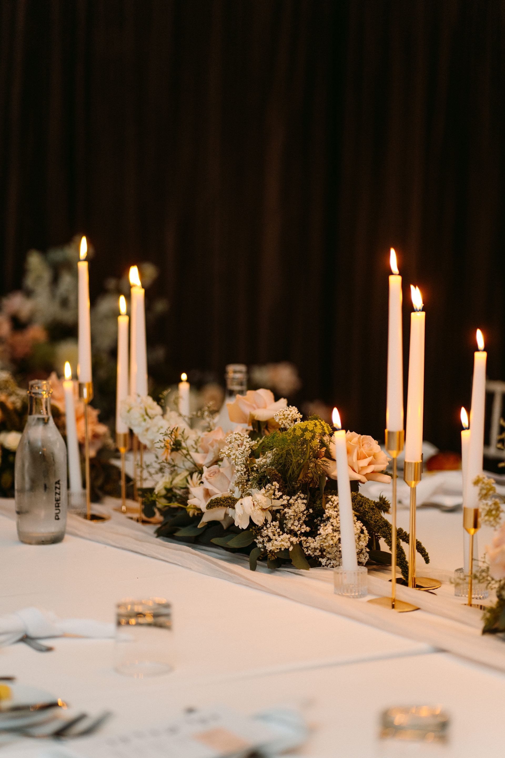 Wedding table centerpiece with lit candles and floral arrangements.