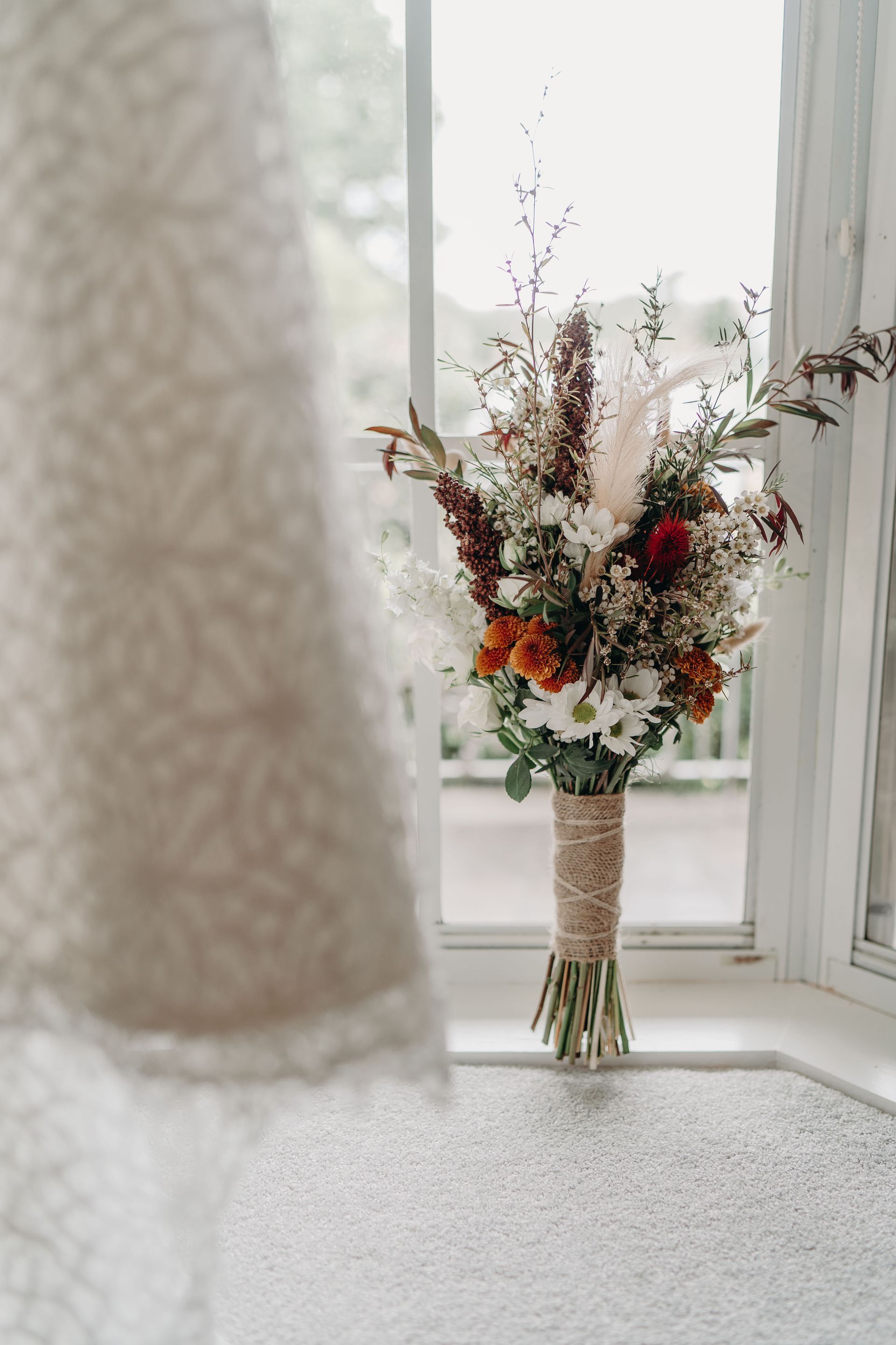 Bouquet of flowers in front of a window, next to lace dress.