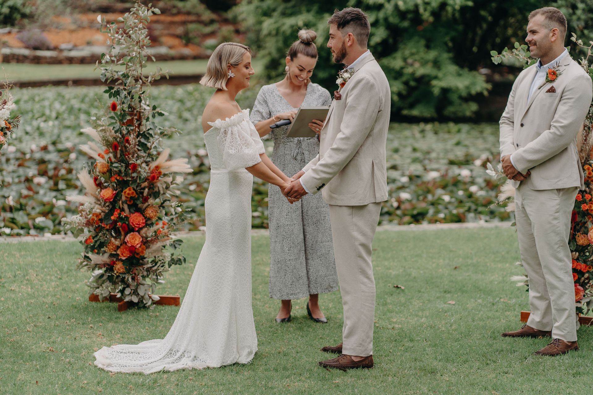 Bride and groom holding hands during outdoor wedding ceremony, officiant reads.