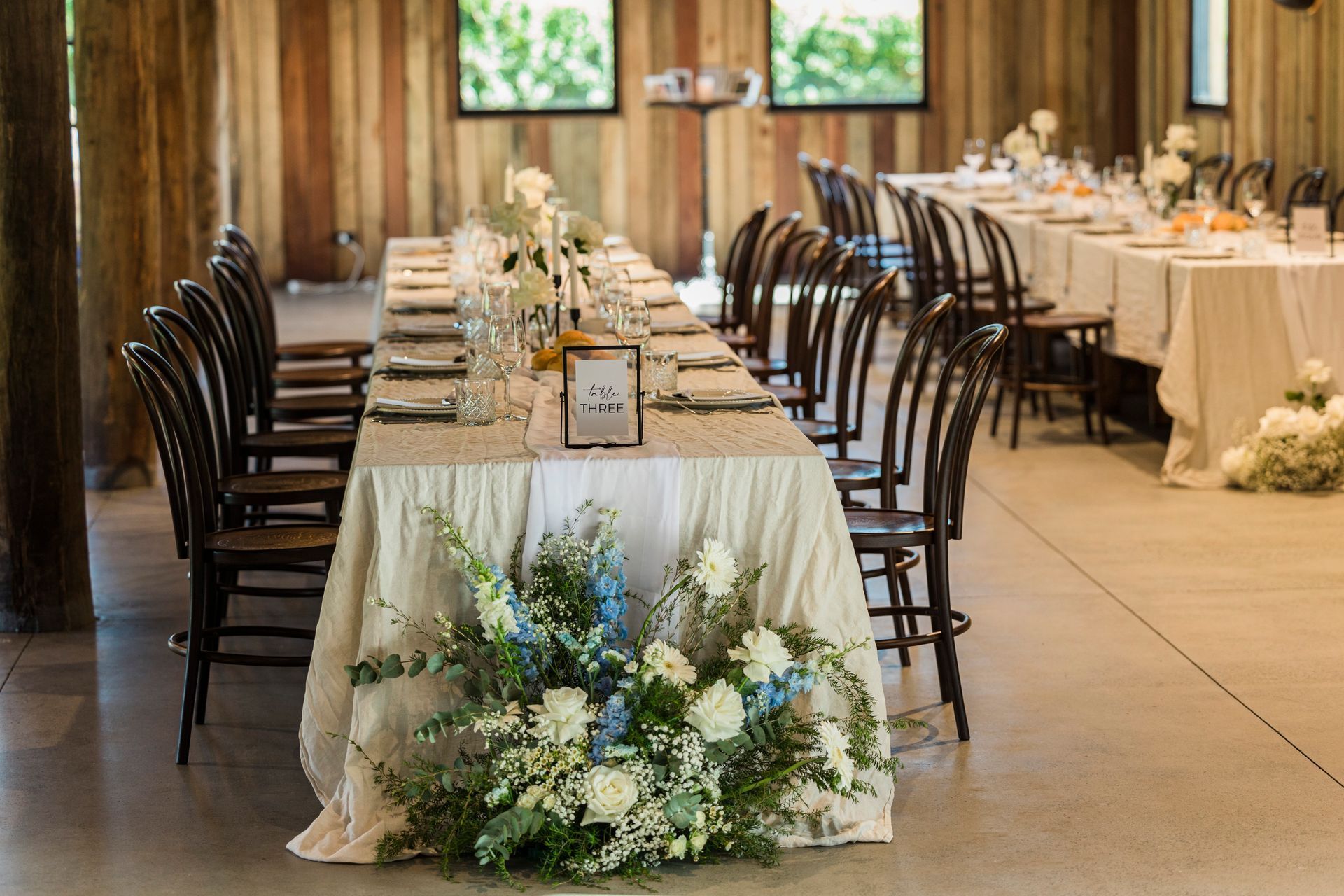 Long table set for a wedding reception in a rustic barn with floral arrangements.