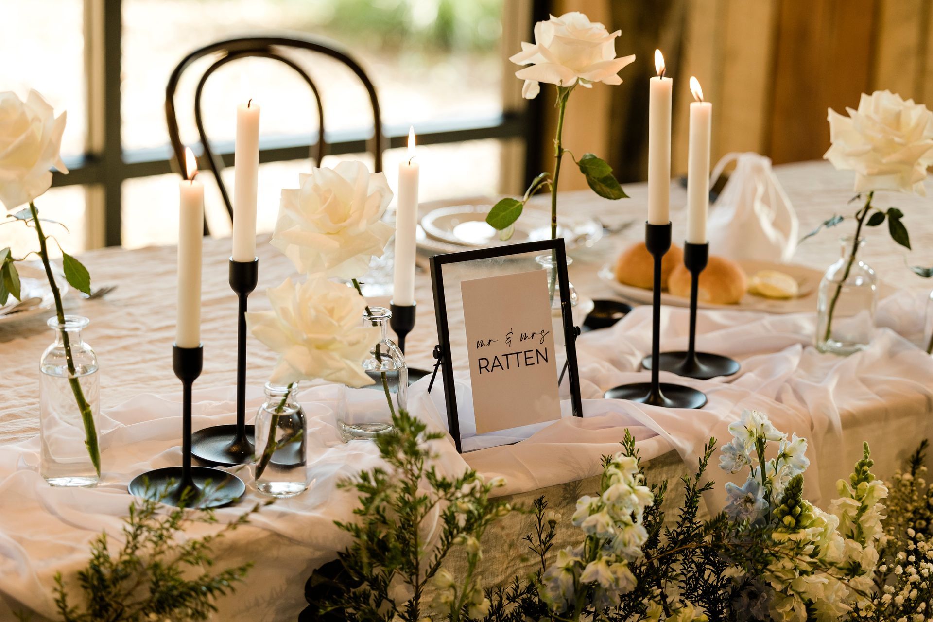 Elegant table setting with white flowers, candles, and a sign.