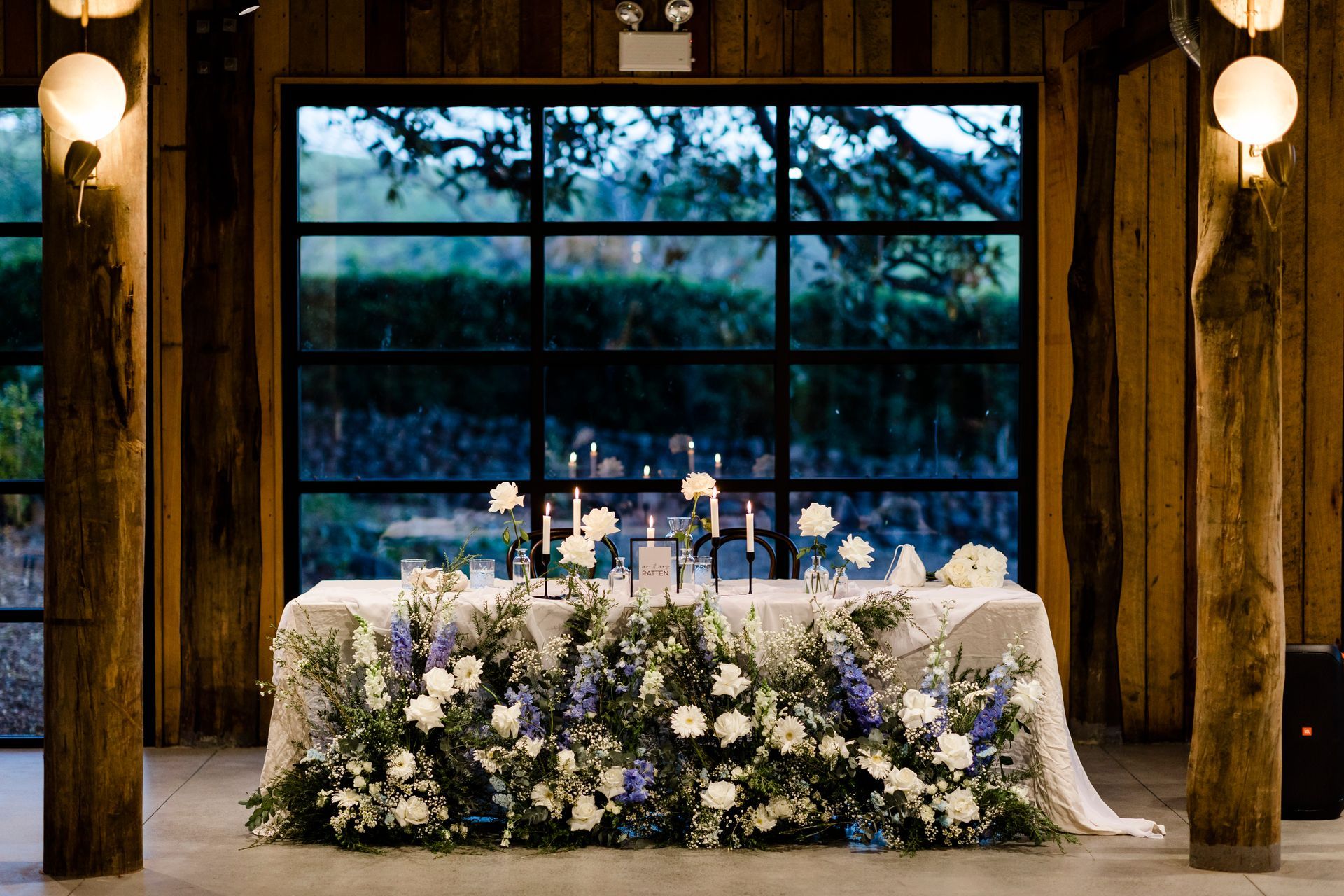 Wedding reception table decorated with flowers and candles, in front of a window overlooking a scenic view.