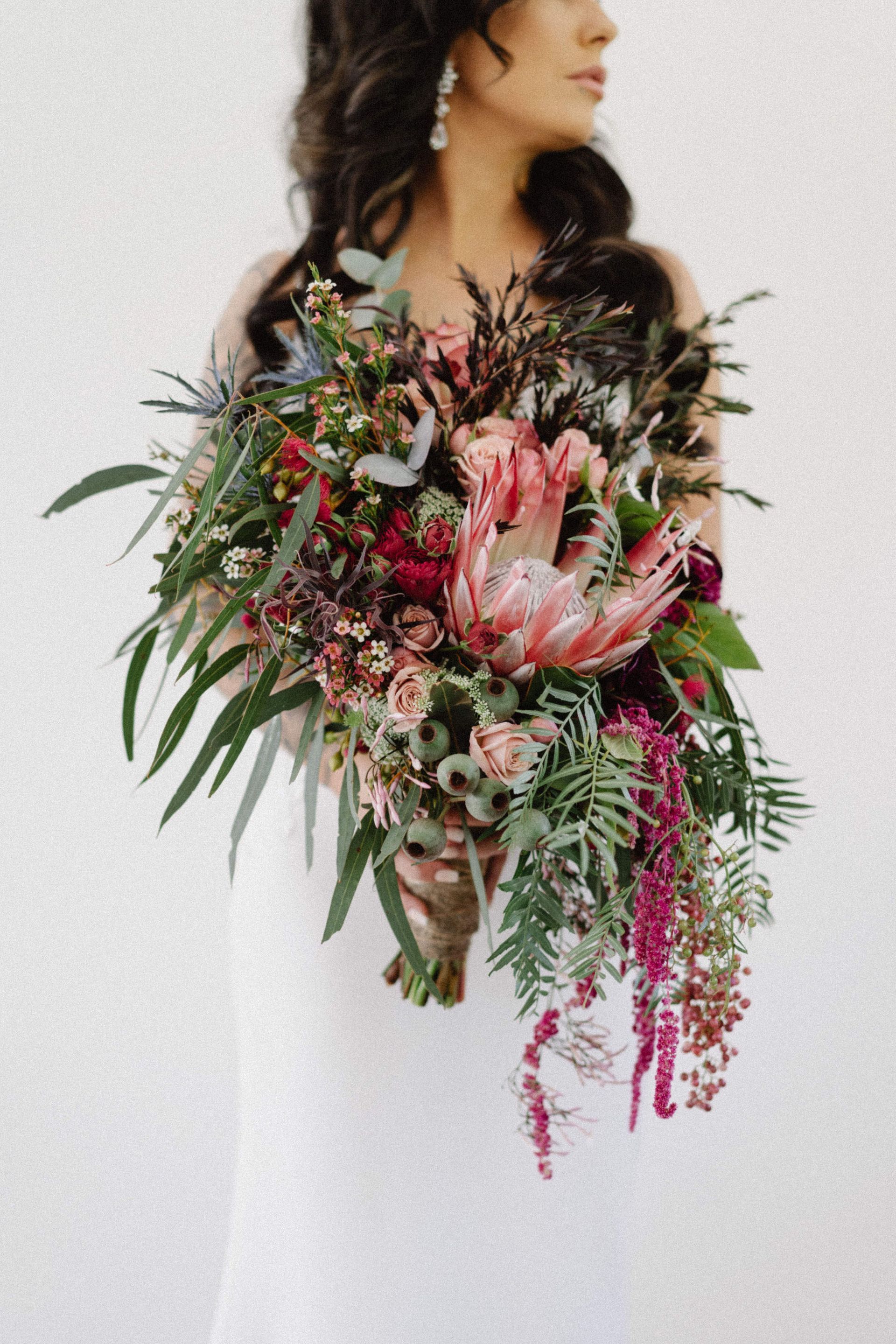 Bride holding an overflowing bouquet of pink and burgundy flowers and greenery.