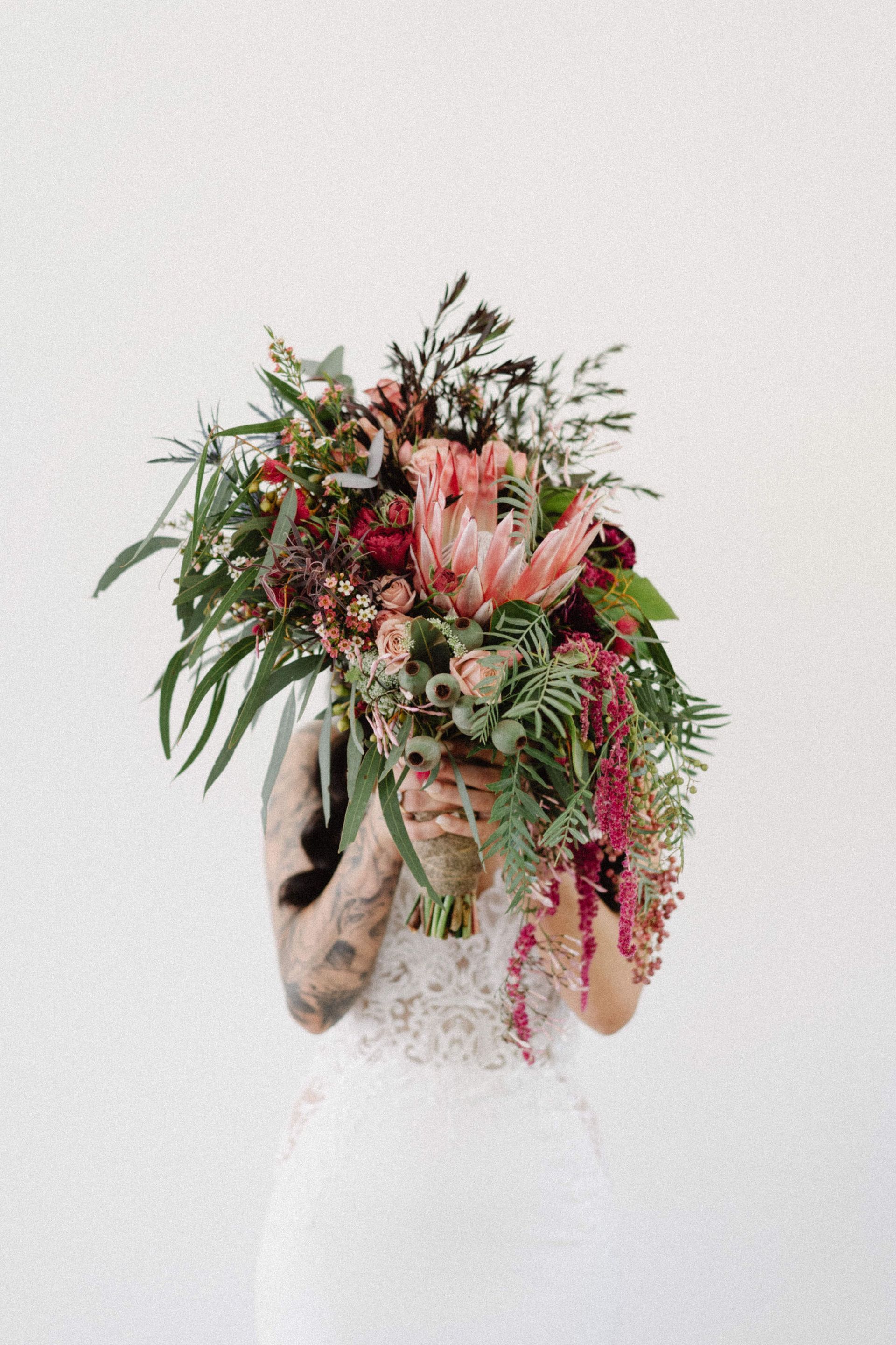 Woman holding a large bouquet with pink and red flowers, wearing a white dress, against a white background.