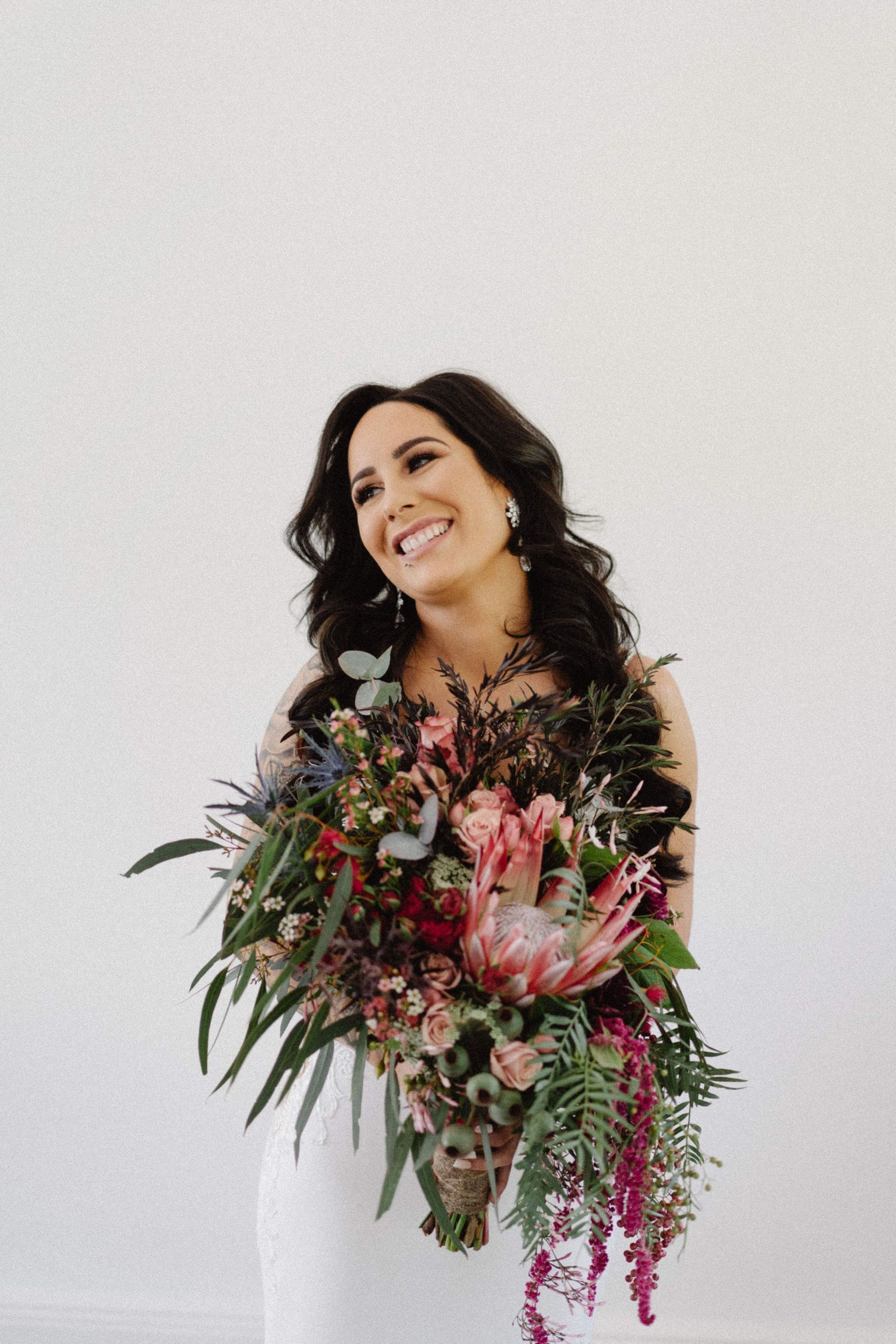 Bride smiling, holding a colorful bouquet, against a white background.