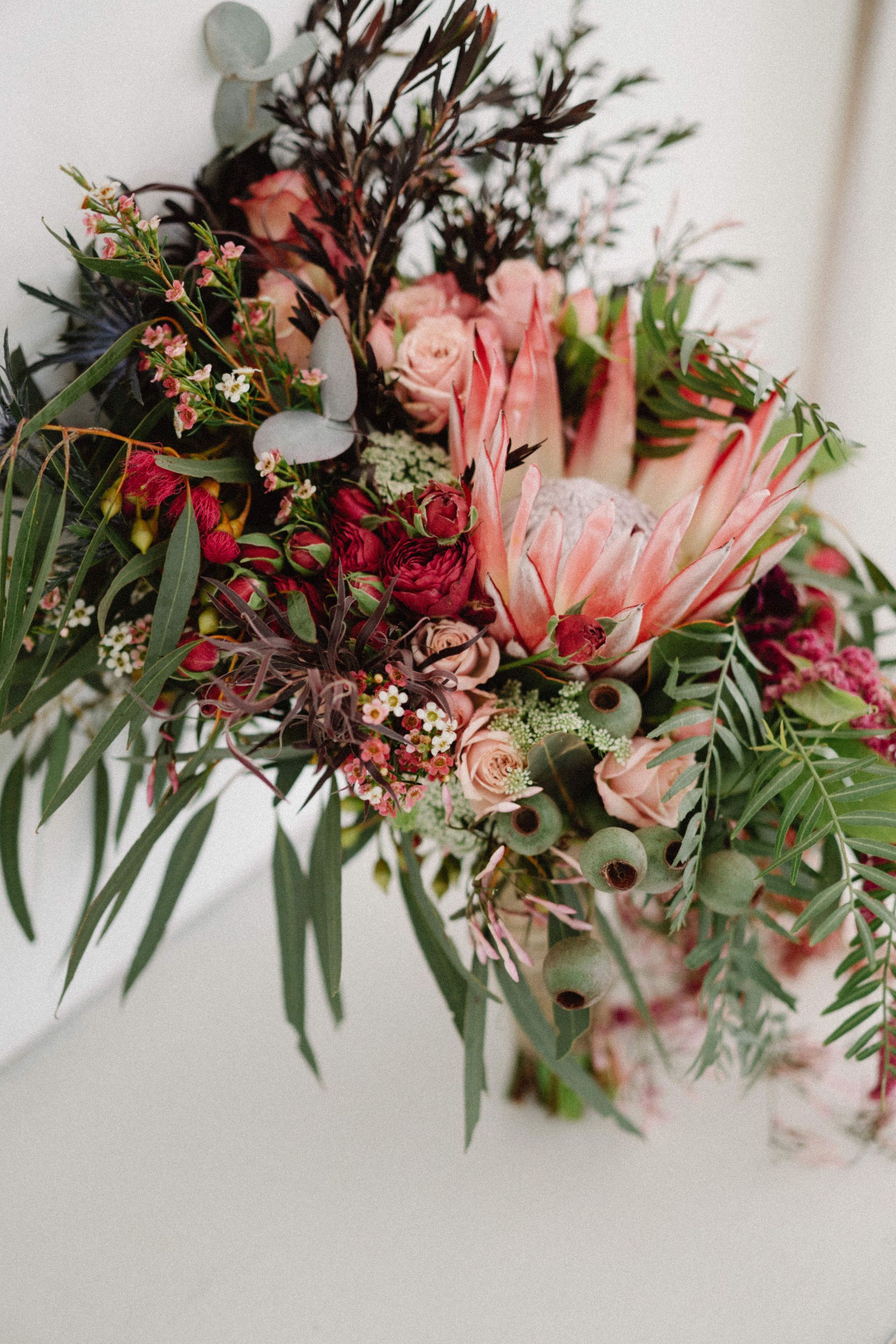 Bouquet of pink protea, roses, and greenery against a white background.