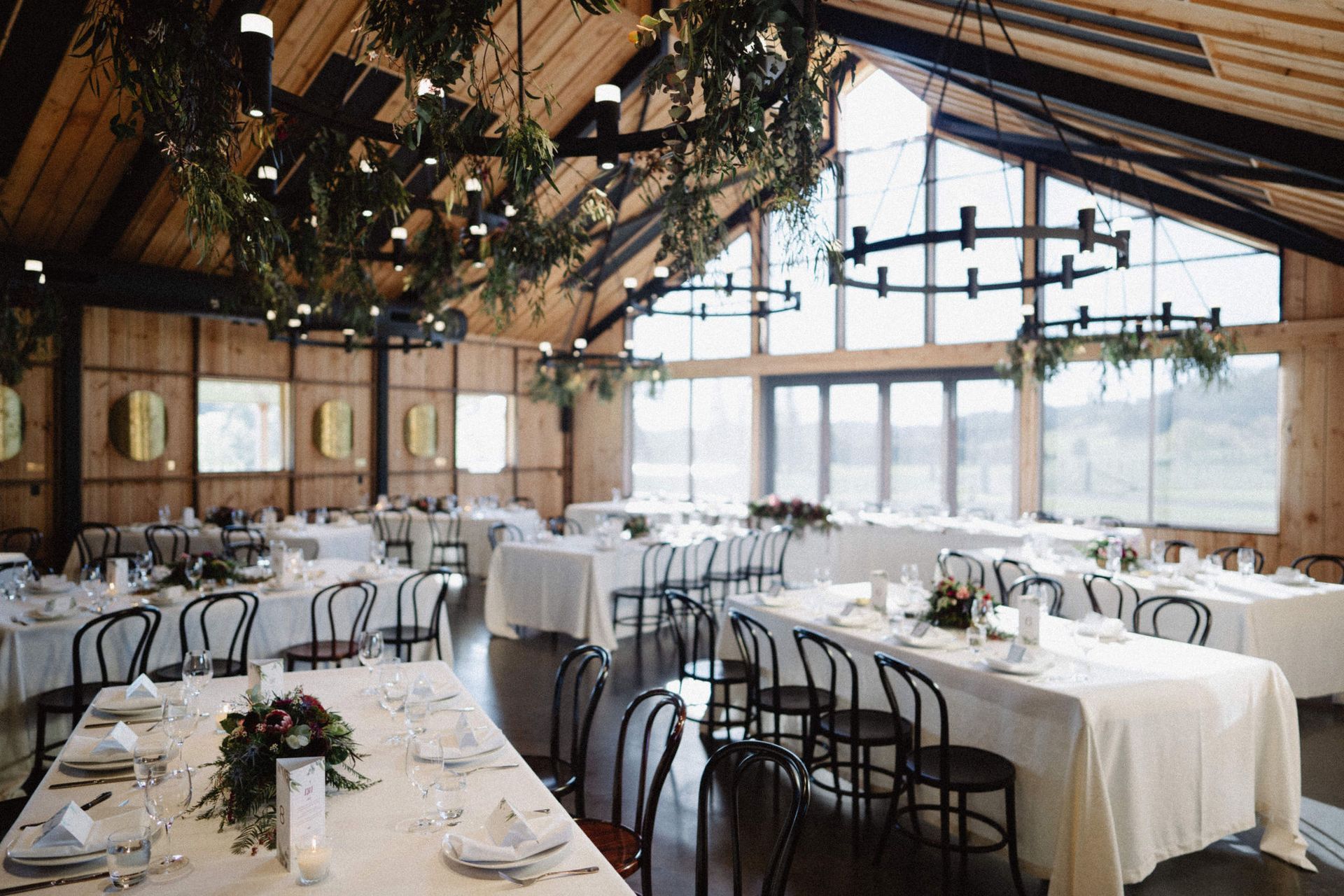 Wedding reception hall with white tablecloths, black chairs, and hanging chandeliers.