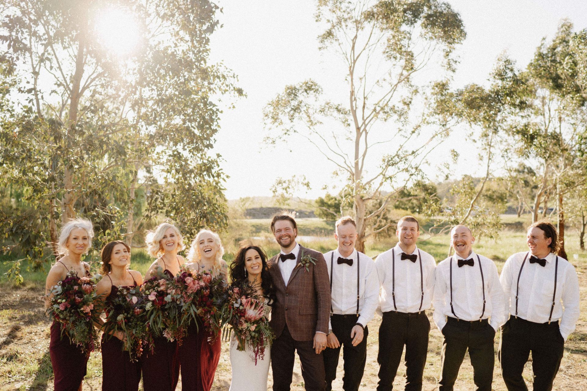 Wedding party: Bride and groom with bridesmaids and groomsmen in a sunny outdoor setting.