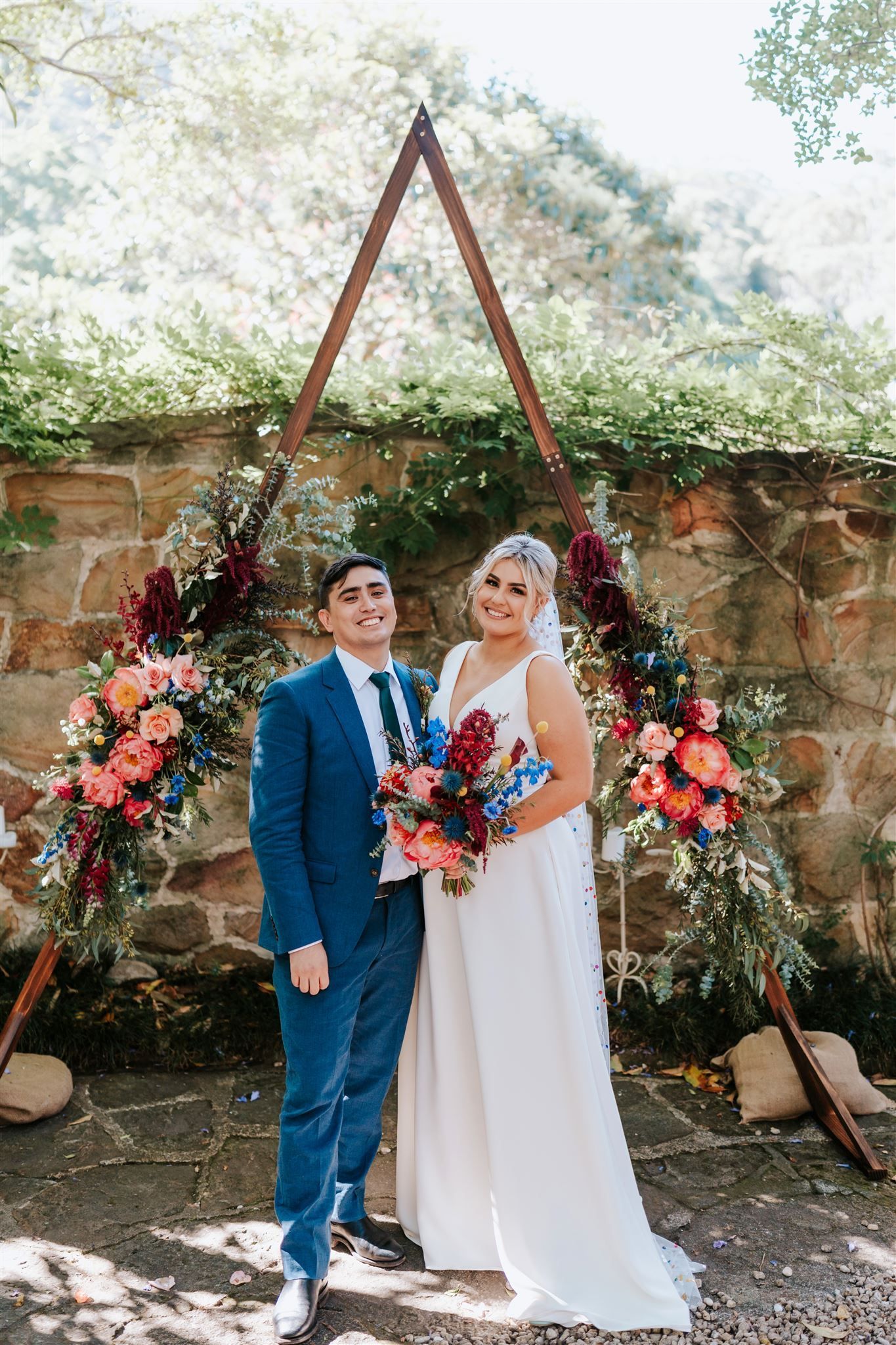 Couple poses for wedding photo under floral arch.