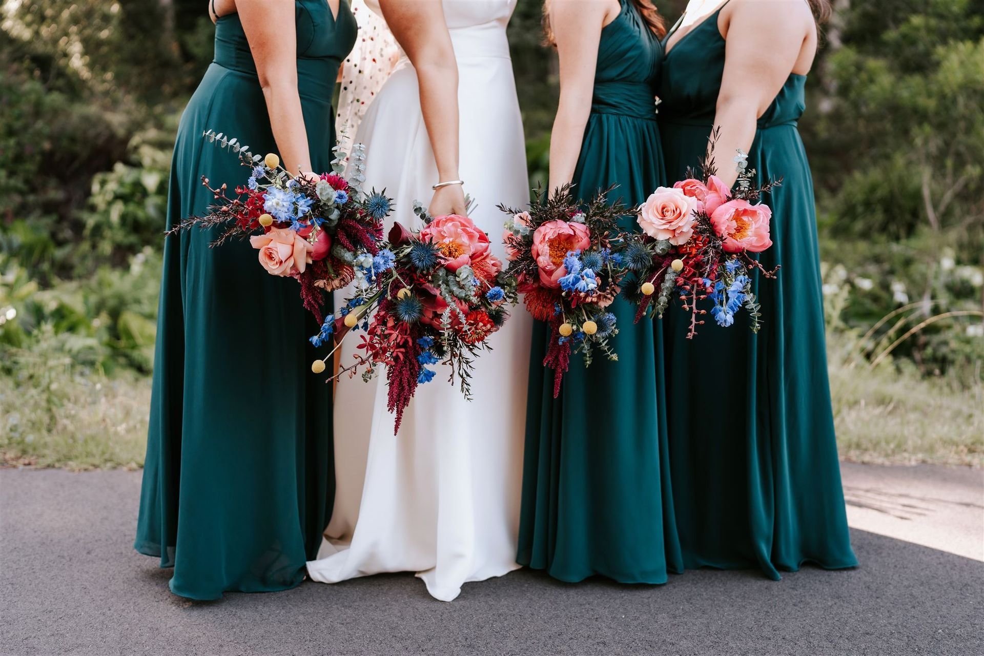 Bride in white gown surrounded by teal bridesmaids holding colorful bouquets.