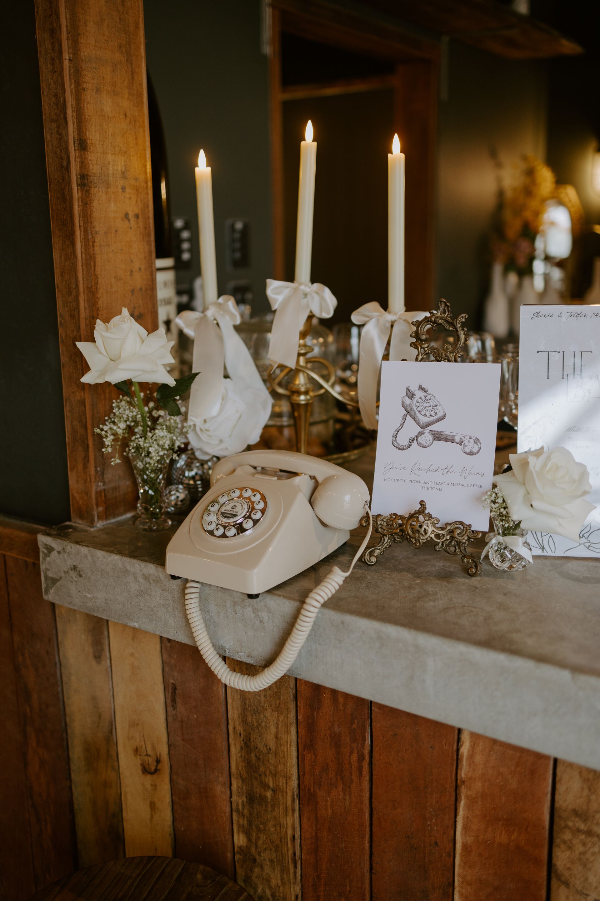 Cream-colored telephone, candles, and floral arrangement on a rustic wooden surface; wedding decor.