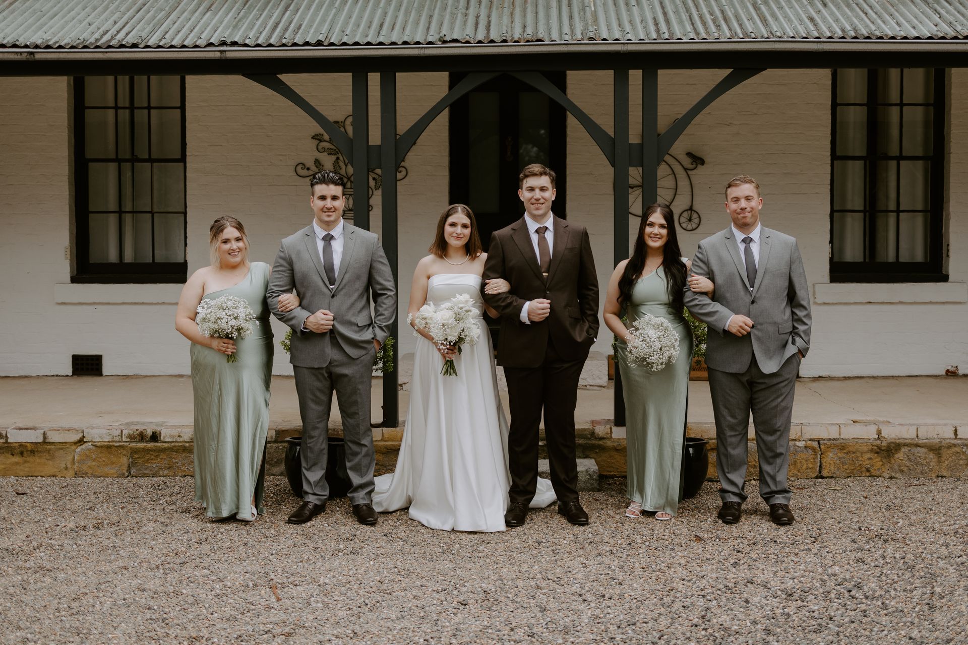 Wedding party posing in front of a white building with dark trim. People are smiling.