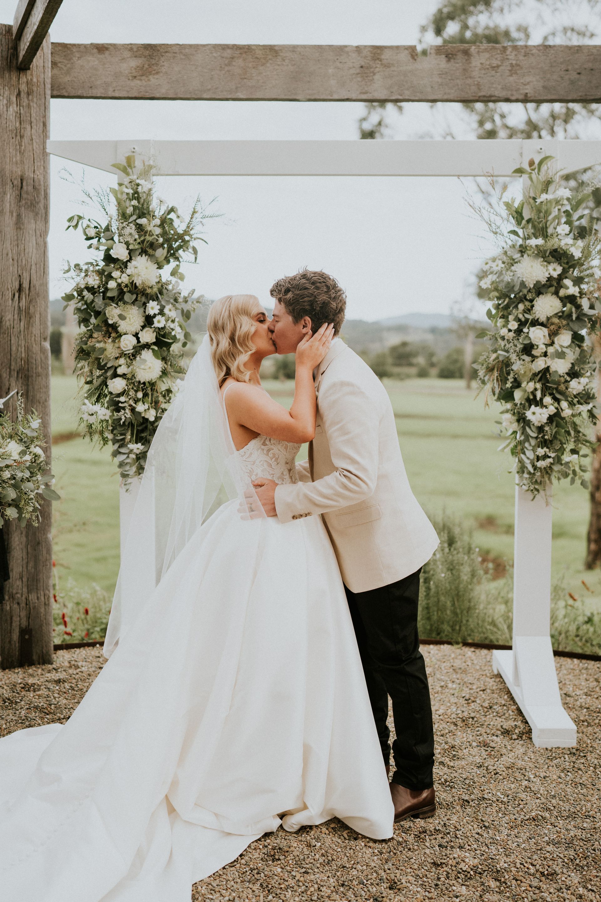 Couple kissing at outdoor wedding ceremony under floral arch.