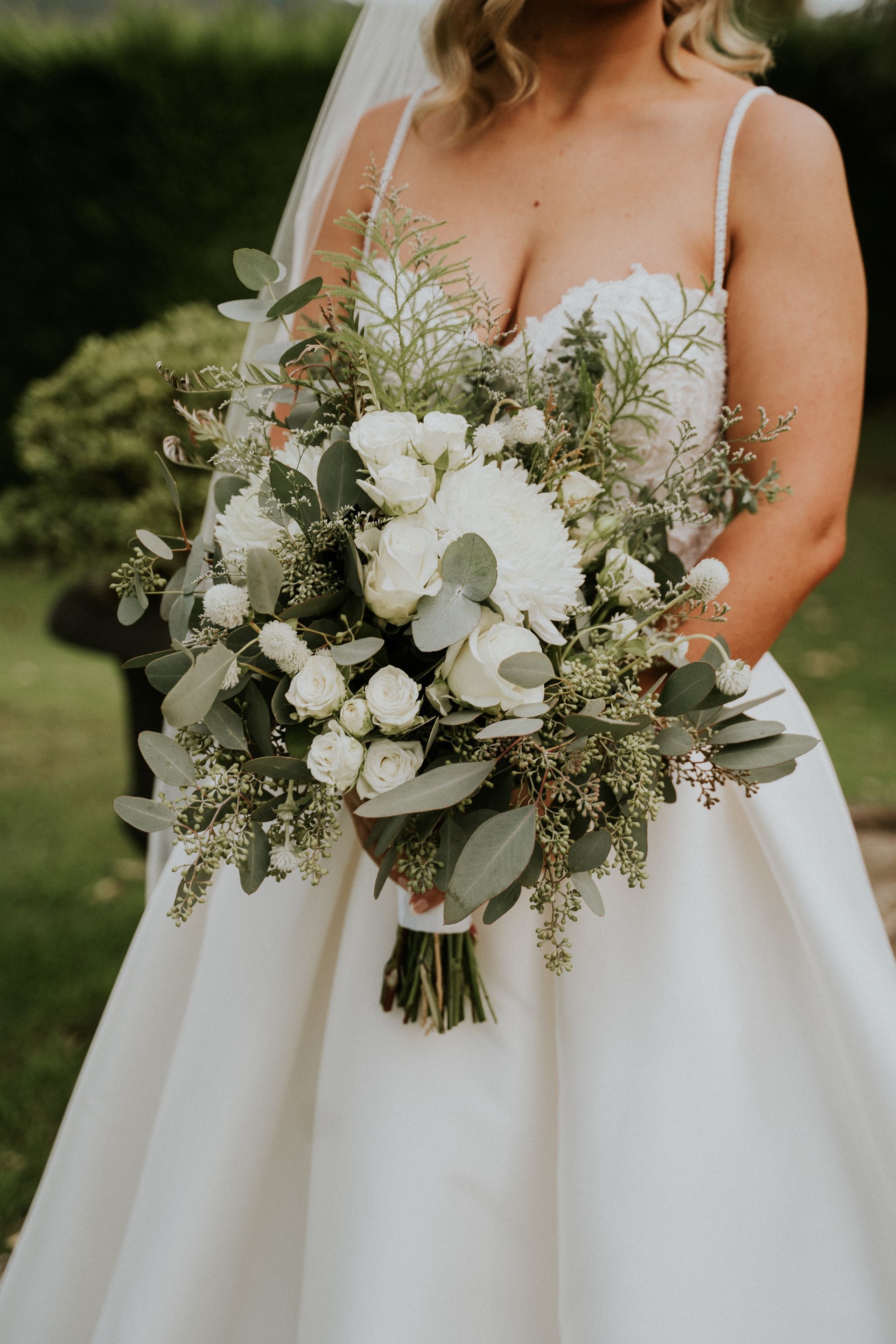 Bride in white dress holding a bouquet of white flowers and greenery.