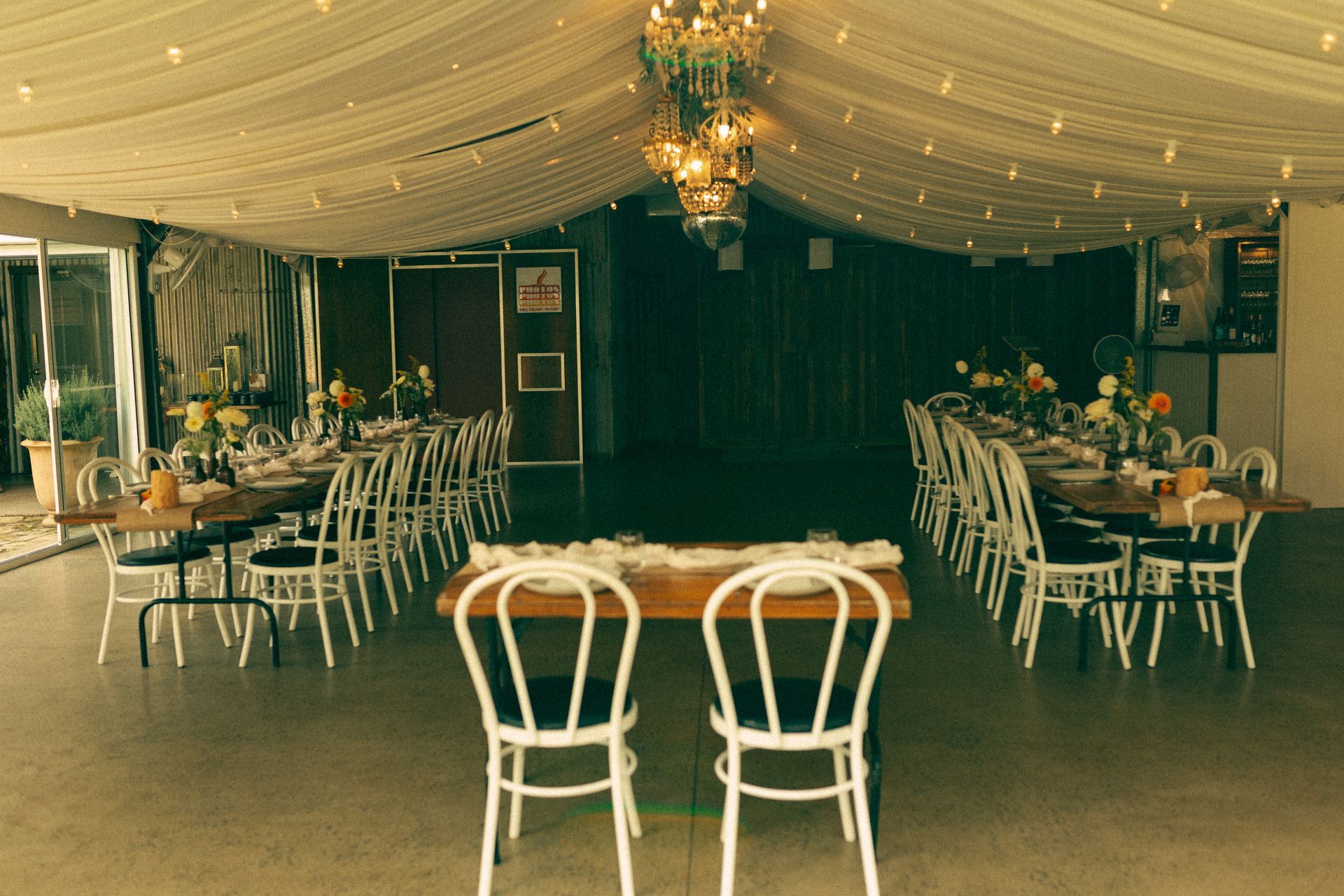 Event space with tables set for a meal, decorated with lights and flowers; two chairs face the tables.