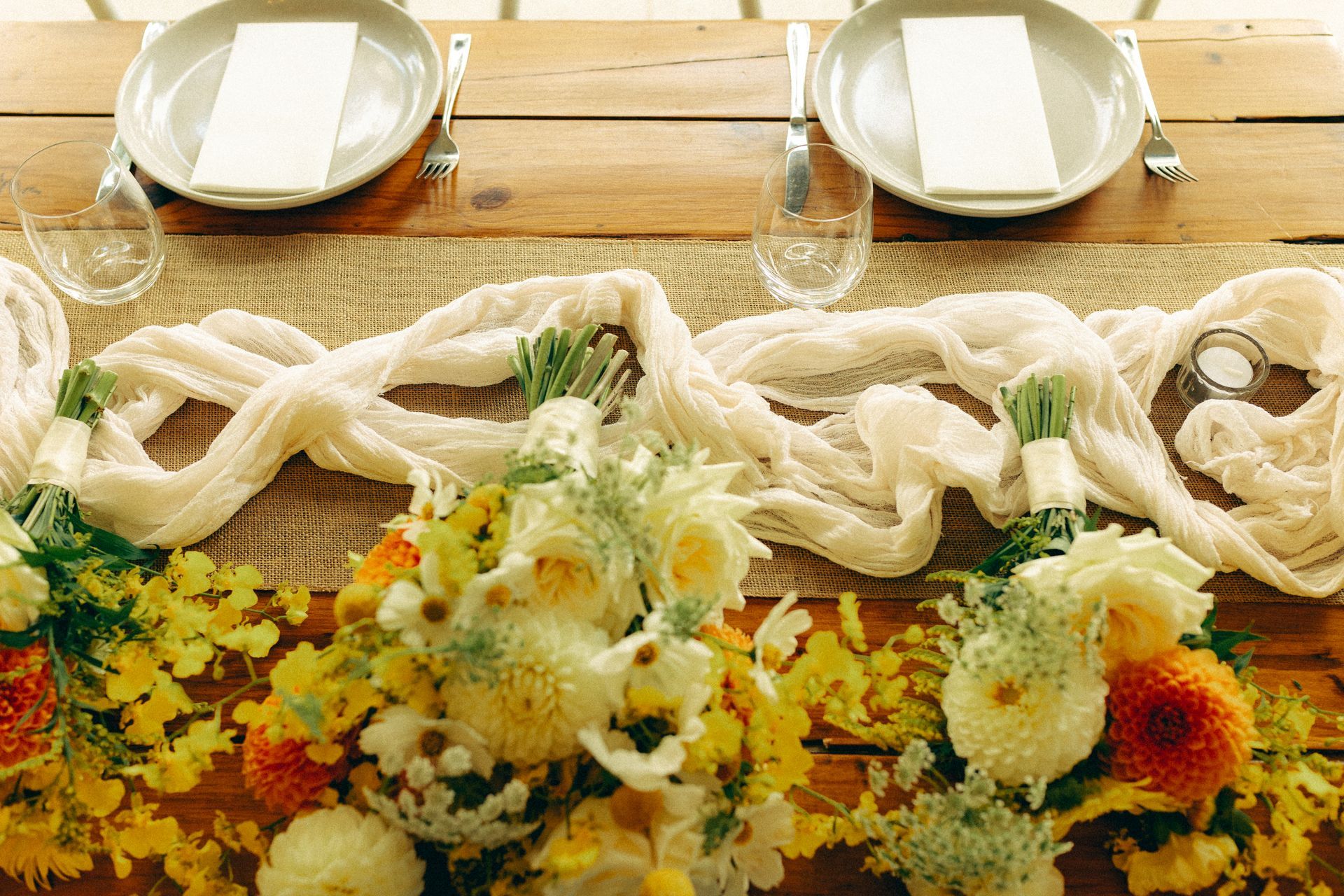 Wedding table setting with flowers, beige cloth, plates, and cutlery on a wooden table.