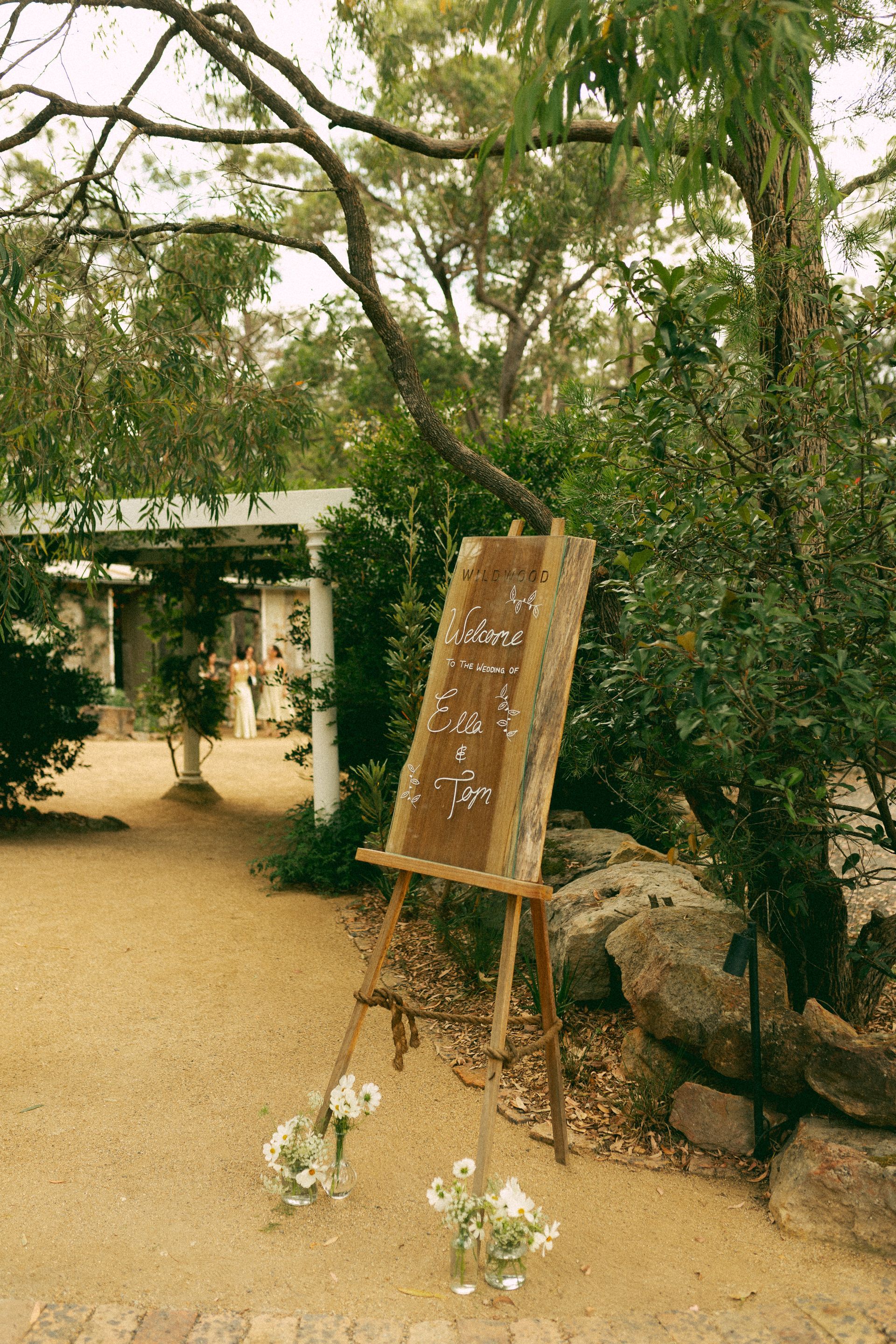 Wooden easel with a guest seating chart outdoors; white flowers at the base.