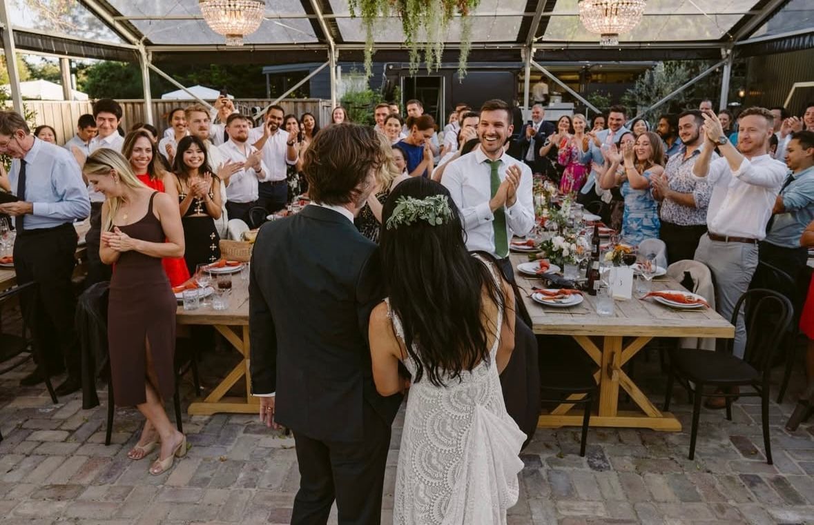 Newlyweds walk through a crowd clapping at an outdoor wedding reception.