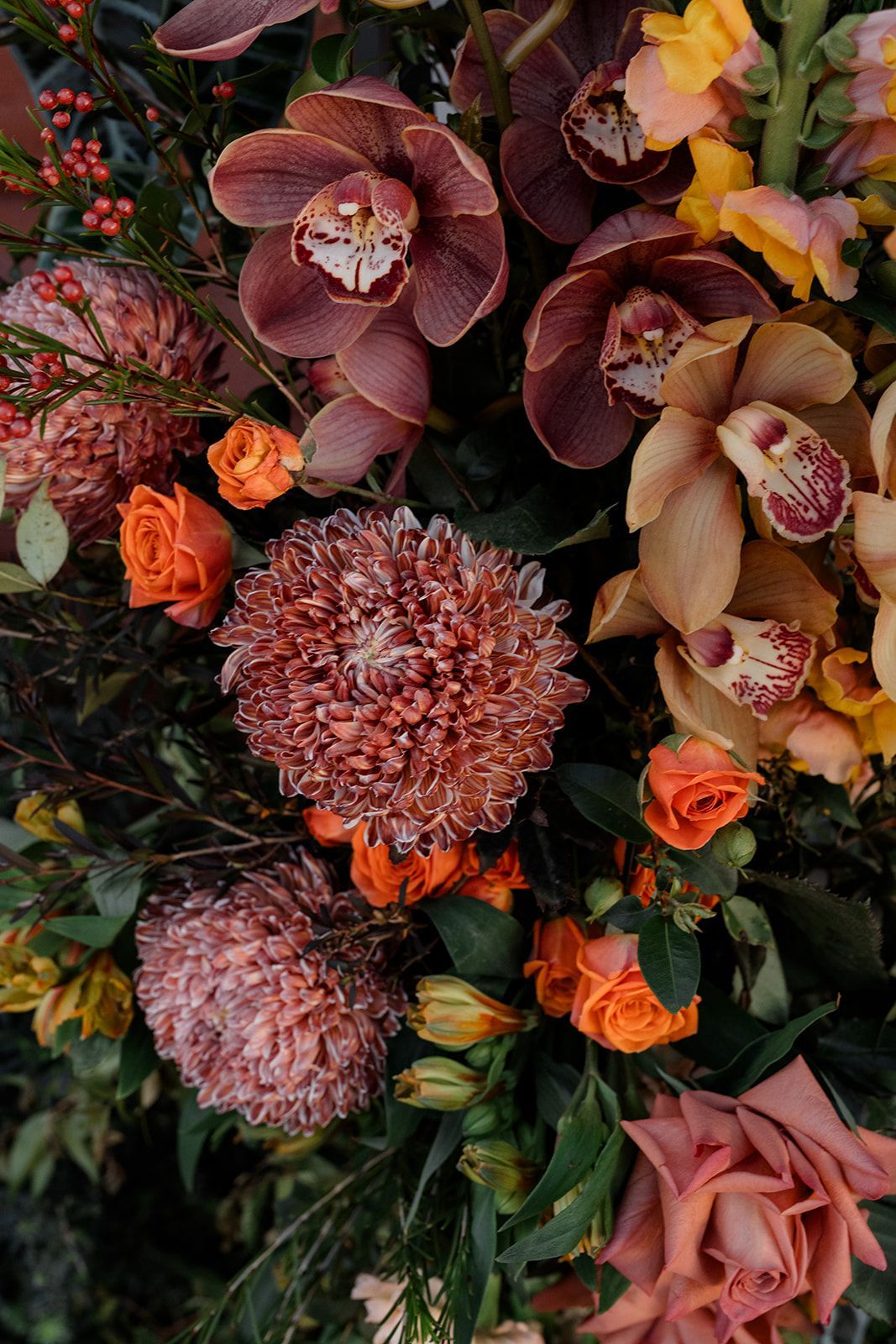 Floral arrangement of rust, orange, and tan flowers, including orchids, roses, and chrysanthemums.