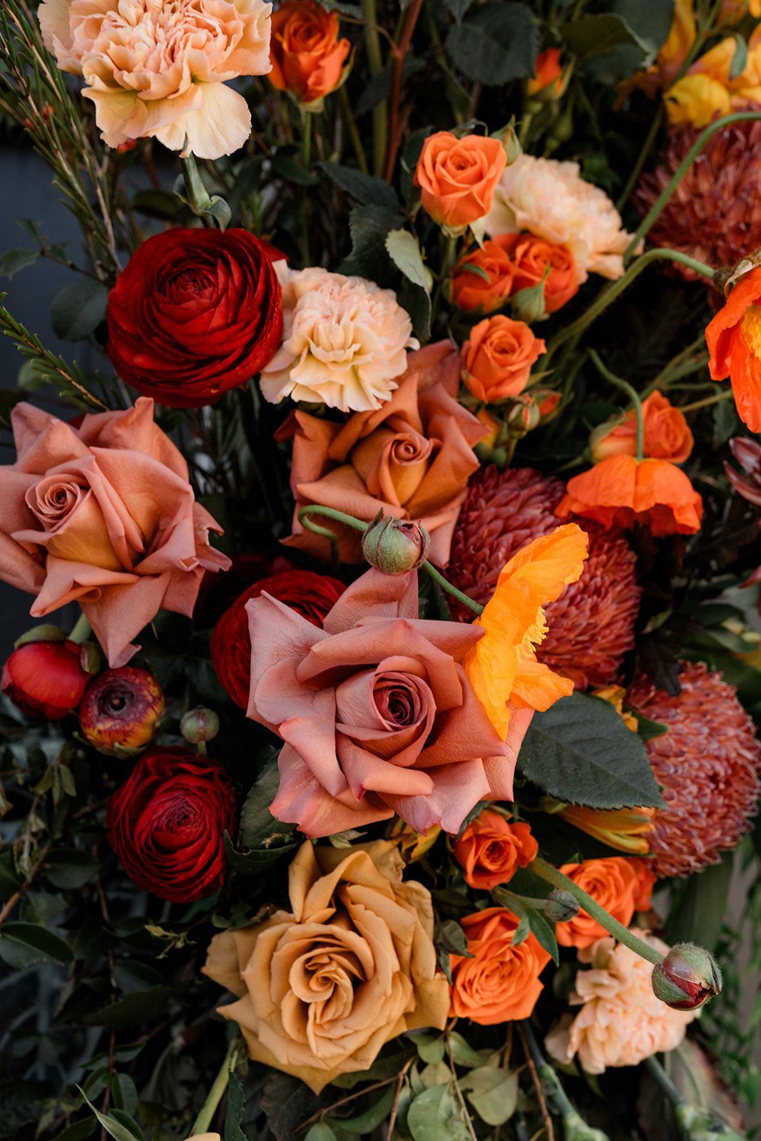 Arrangement of autumnal roses, carnations, and other blooms in shades of orange, red, and peach.