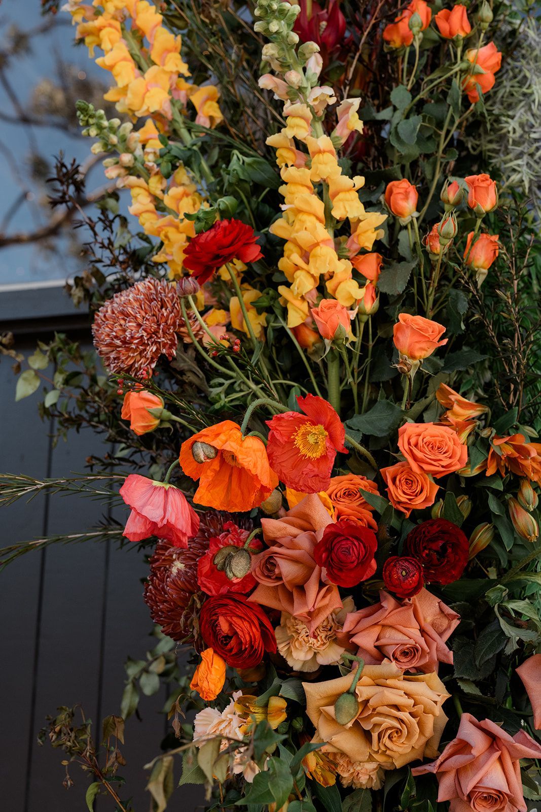 Close-up of a colorful floral arrangement with various orange, red, and yellow flowers, greenery, and foliage.