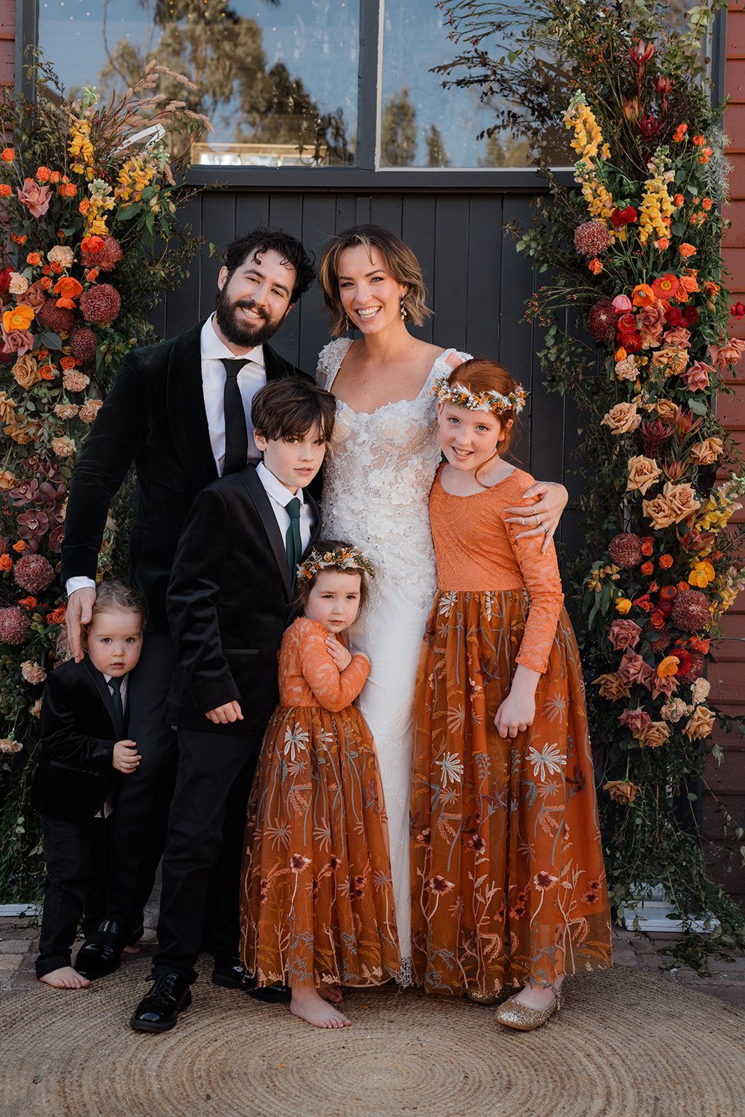 Family portrait with bride, groom, and three children in front of floral archway.