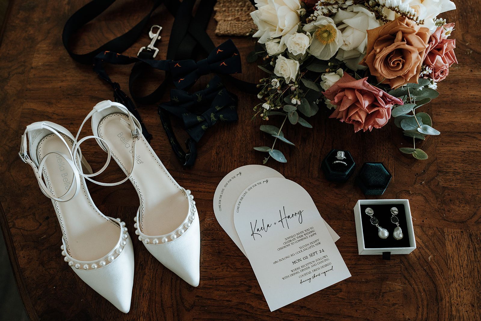 Wedding details: white shoes, bouquet, invitations, jewelry, and garter on a wooden table.