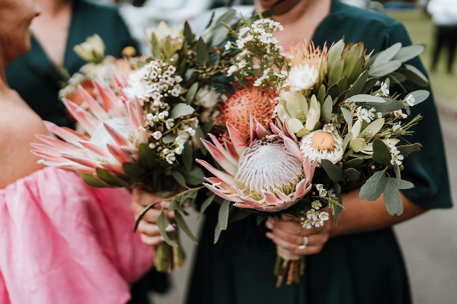 Woman in green dress holds a bouquet of pink and orange protea flowers.
