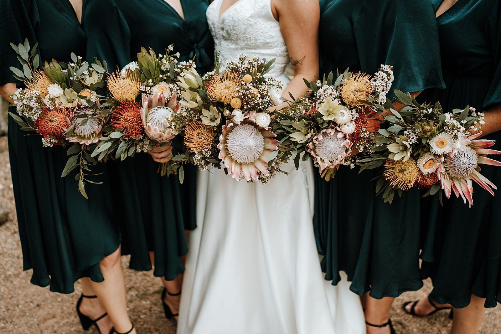 Bride and bridesmaids with long, colorful bouquets, wearing green dresses.