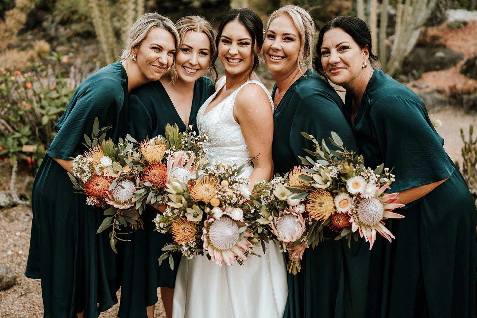 Bride and bridesmaids in teal dresses, holding bouquets, smiling outdoors.