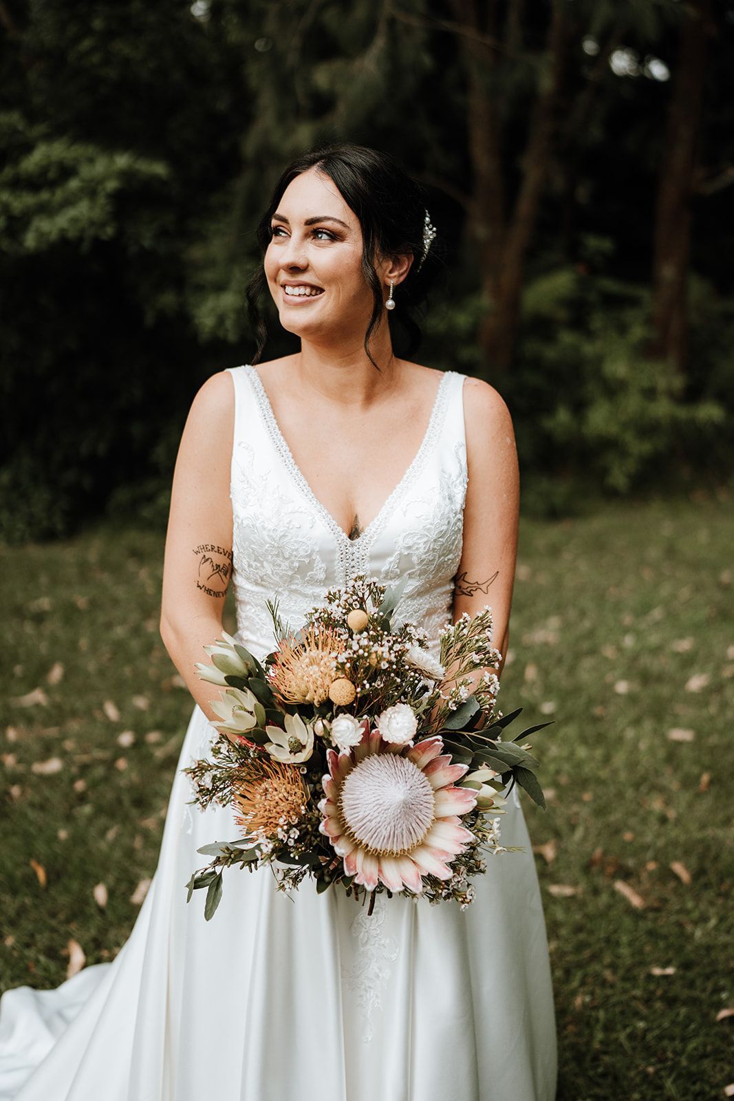 Bride in white dress, holding bouquet, smiling outdoors.