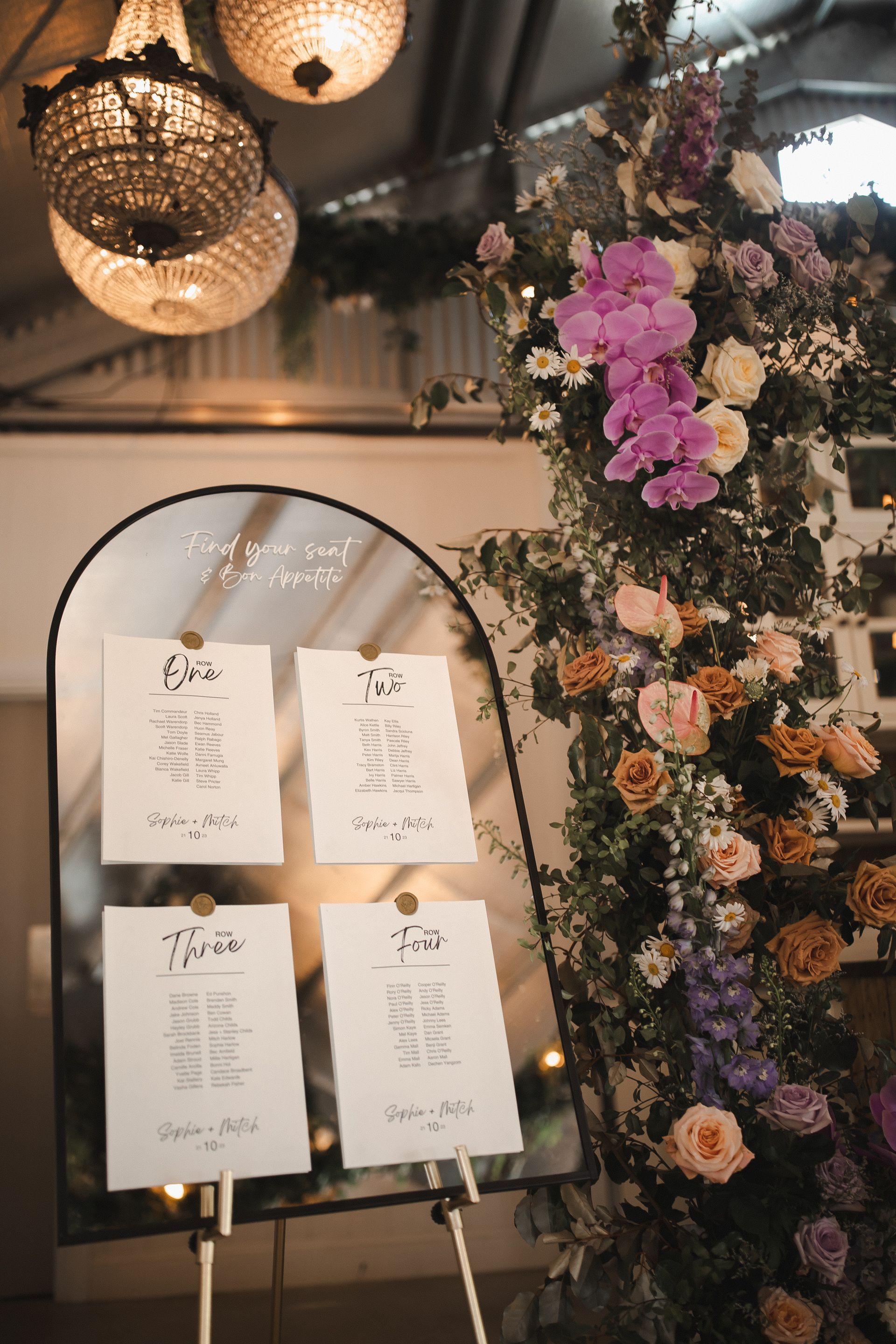Wedding seating chart display with floral archway and chandeliers.