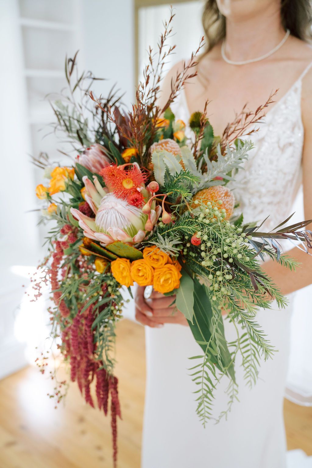 Bride holding colorful floral bouquet, featuring protea and cascading red amaranthus.