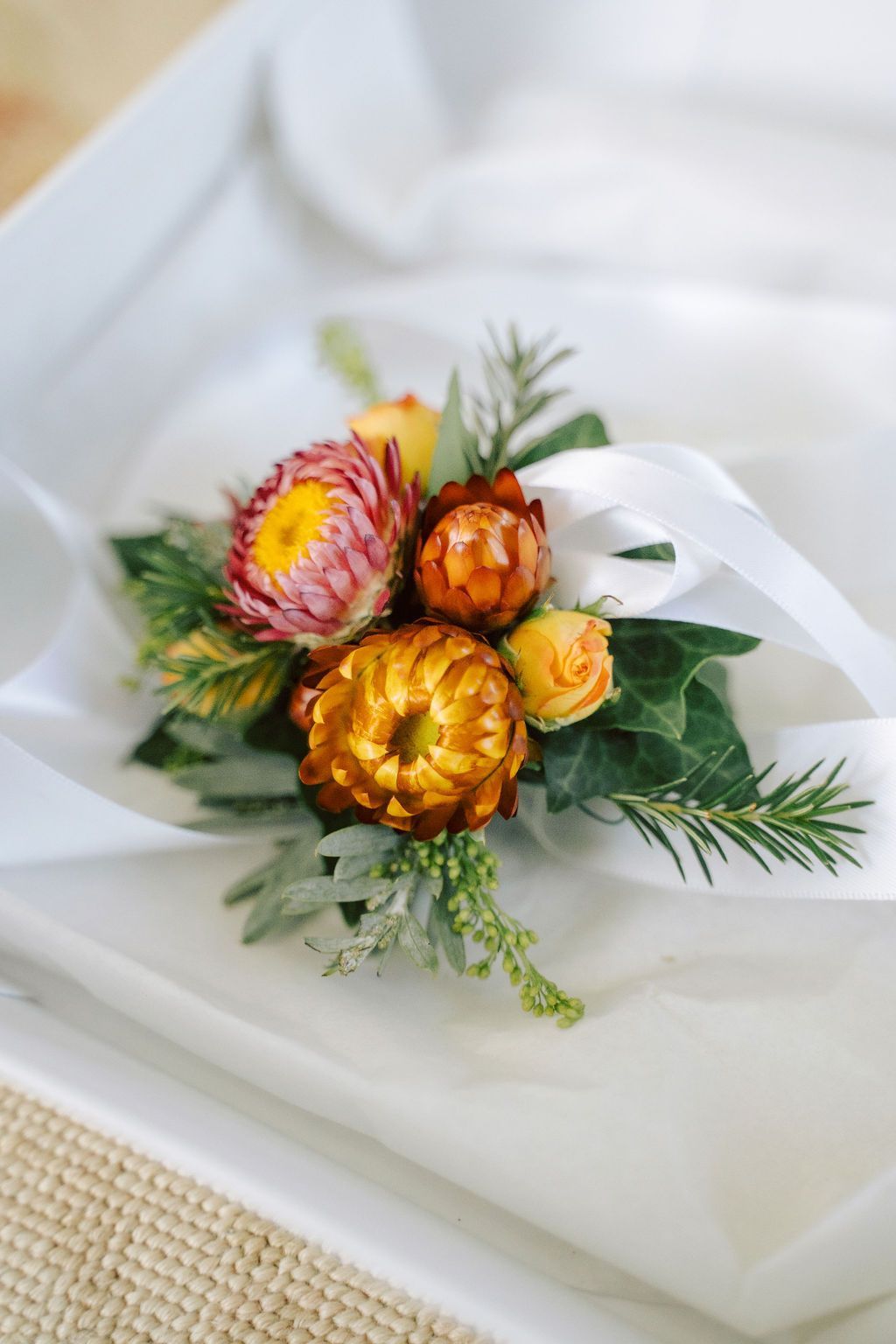 Corsage of colorful dried flowers and greenery on white fabric.