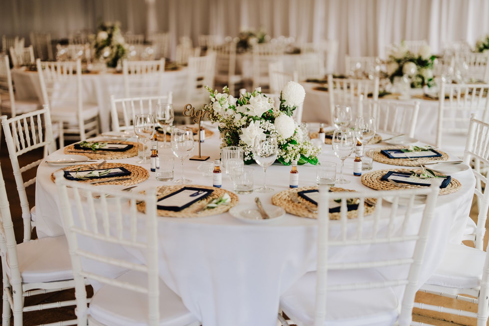 Wedding reception table setting with white linens, flowers, and place settings.