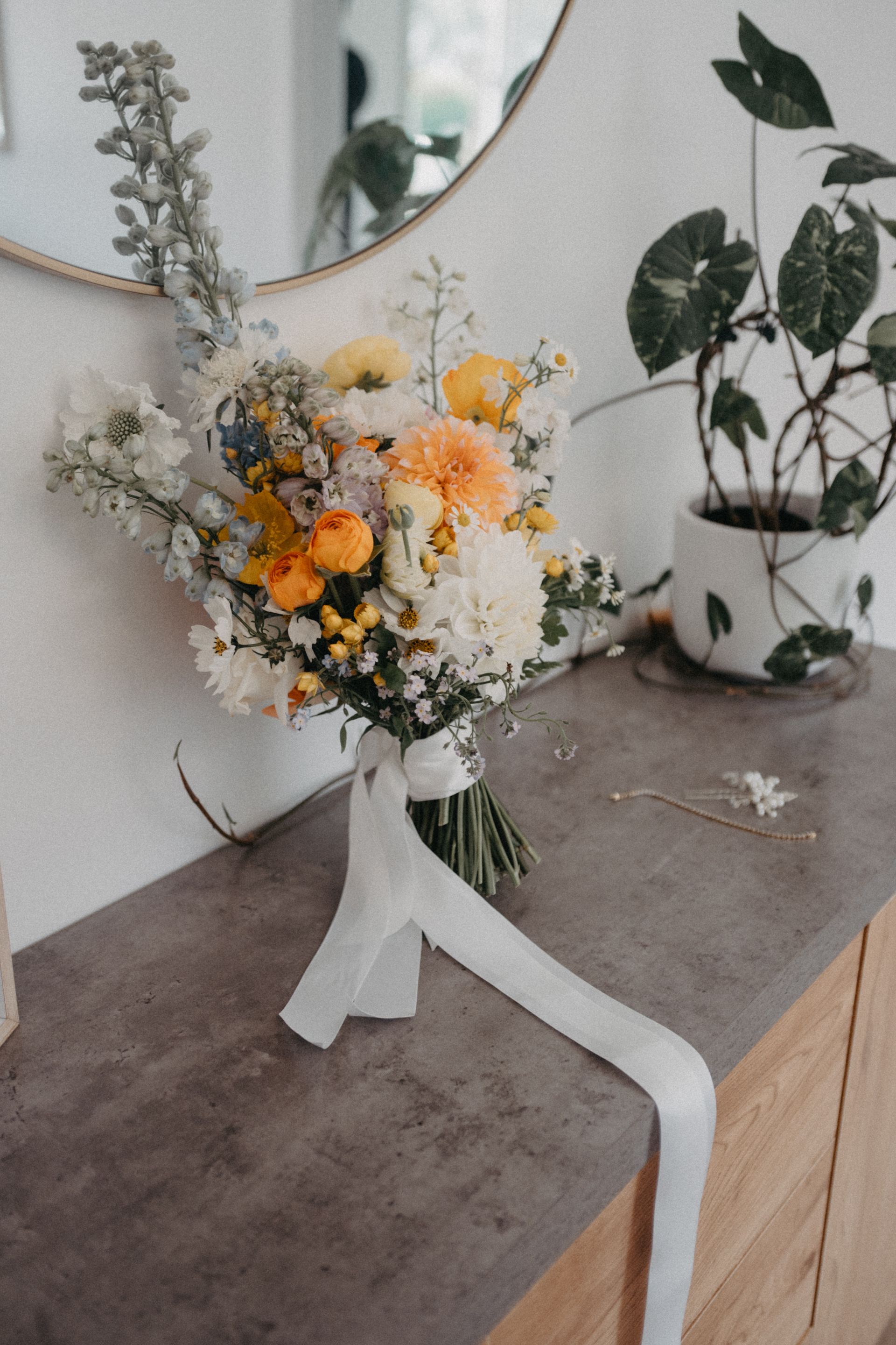 Bouquet of yellow and white flowers with a long white ribbon, resting on a wood cabinet.
