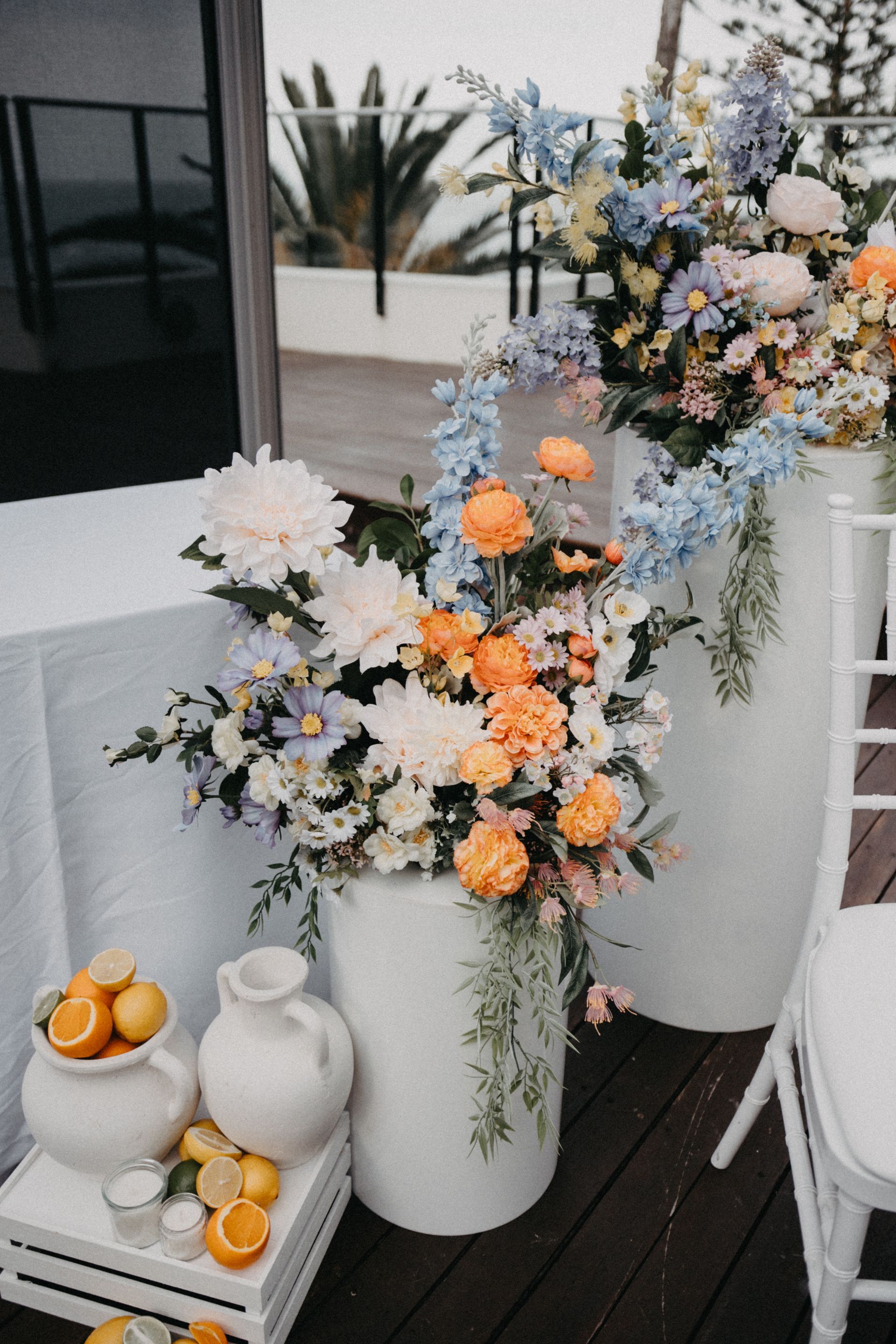 Floral arrangements in white pots with citrus fruit, setting for an outdoor event.