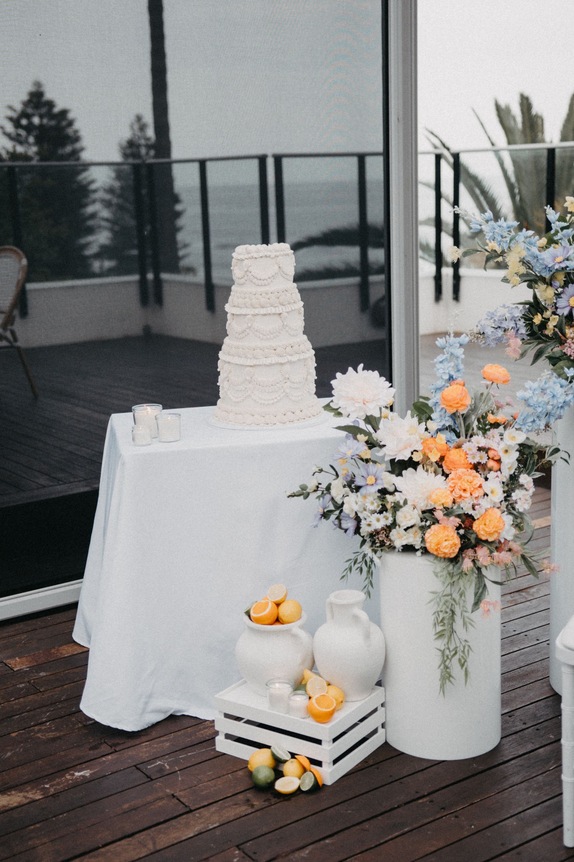 Wedding cake on white table with floral arrangements and lemons. Outdoor ocean view.
